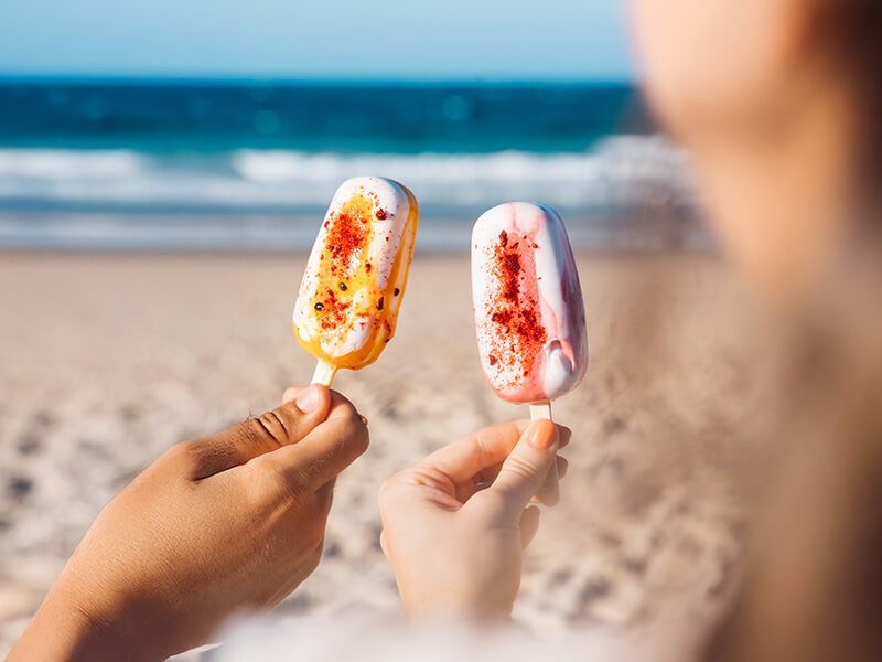 Close-up of two colourful ice creams held at the beach.