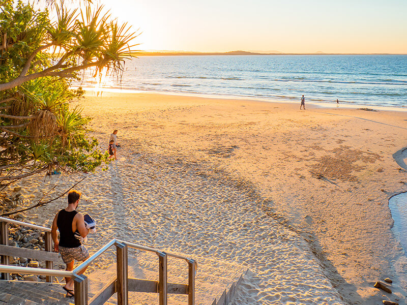 People walking along a sandy Sunshine Coast beach at sunset.