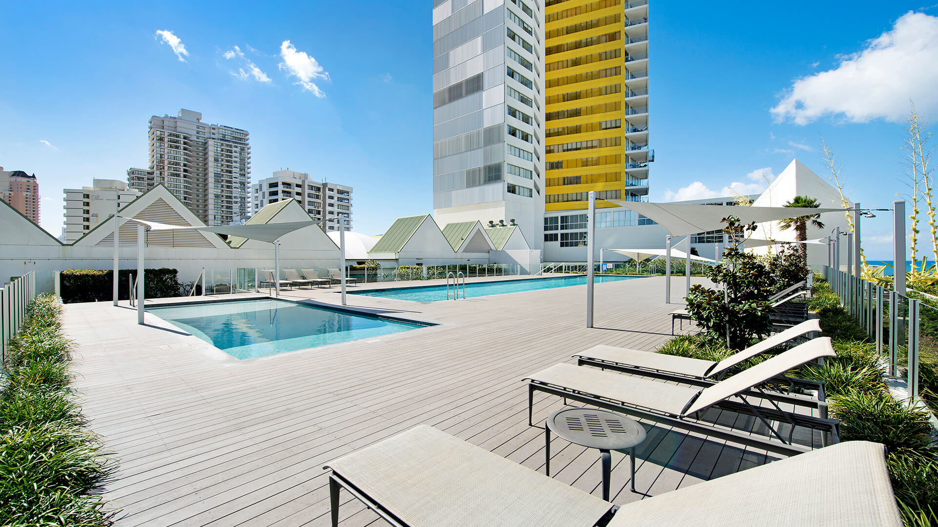Modern pool deck at ULTIQA Air on Broadbeach with shaded lounges, lush greenery, and high-rise city views.