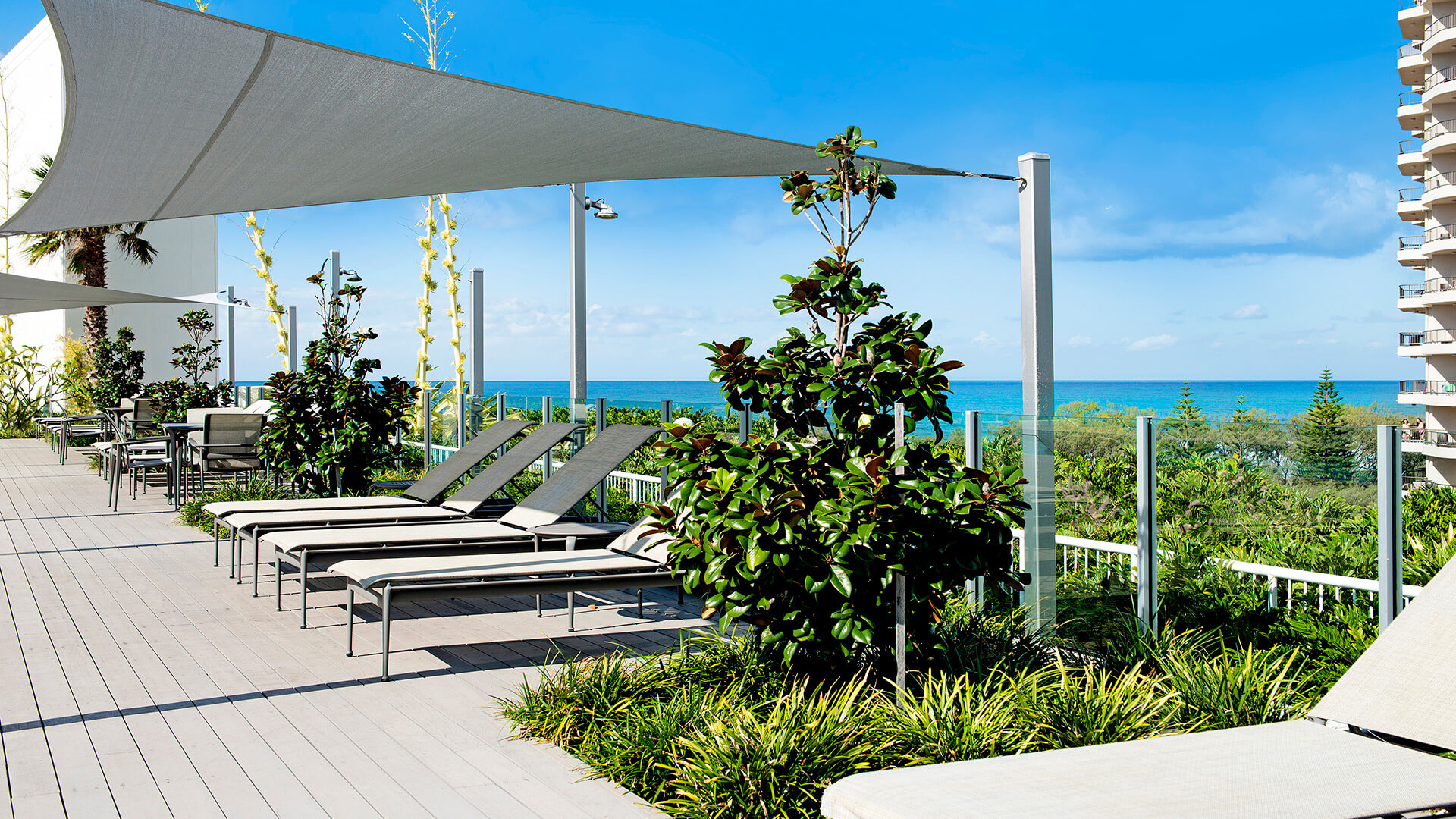 Ocean-view lounge deck at ULTIQA Air on Broadbeach with shaded seating, timber flooring, and lush planters under a clear sky.