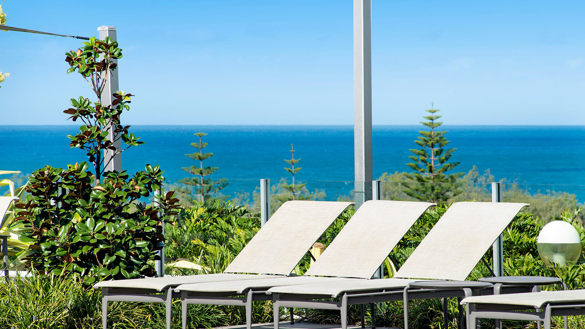 Ocean-facing lounge deck at ULTIQA Air on Broadbeach with sun chairs, tropical greenery, and panoramic sea views under a clear sky.