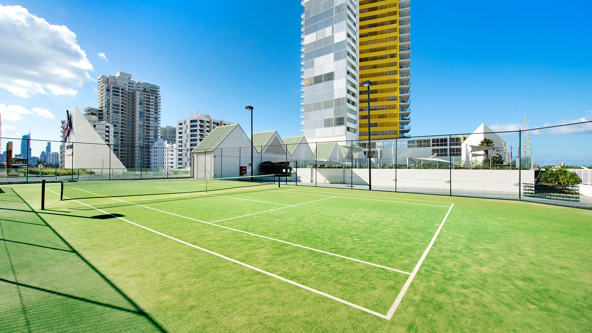 Outdoor tennis court at ULTIQA Air on Broadbeach with green surface, urban high-rise backdrop, and clear skies.