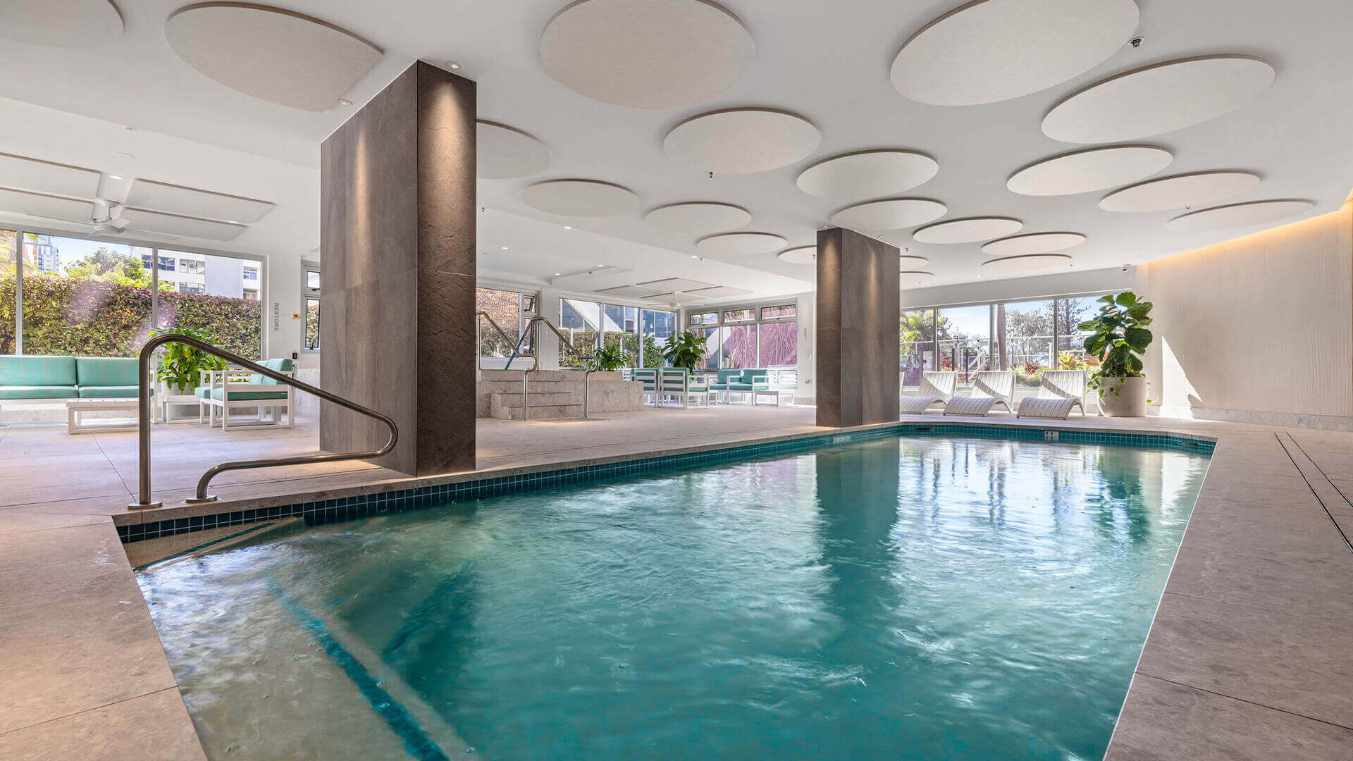 Indoor leisure pool area at ULTIQA Beach Haven featuring a heated lap pool, spa, lounge seating, and modern design — ideal for relaxation and year-round enjoyment.