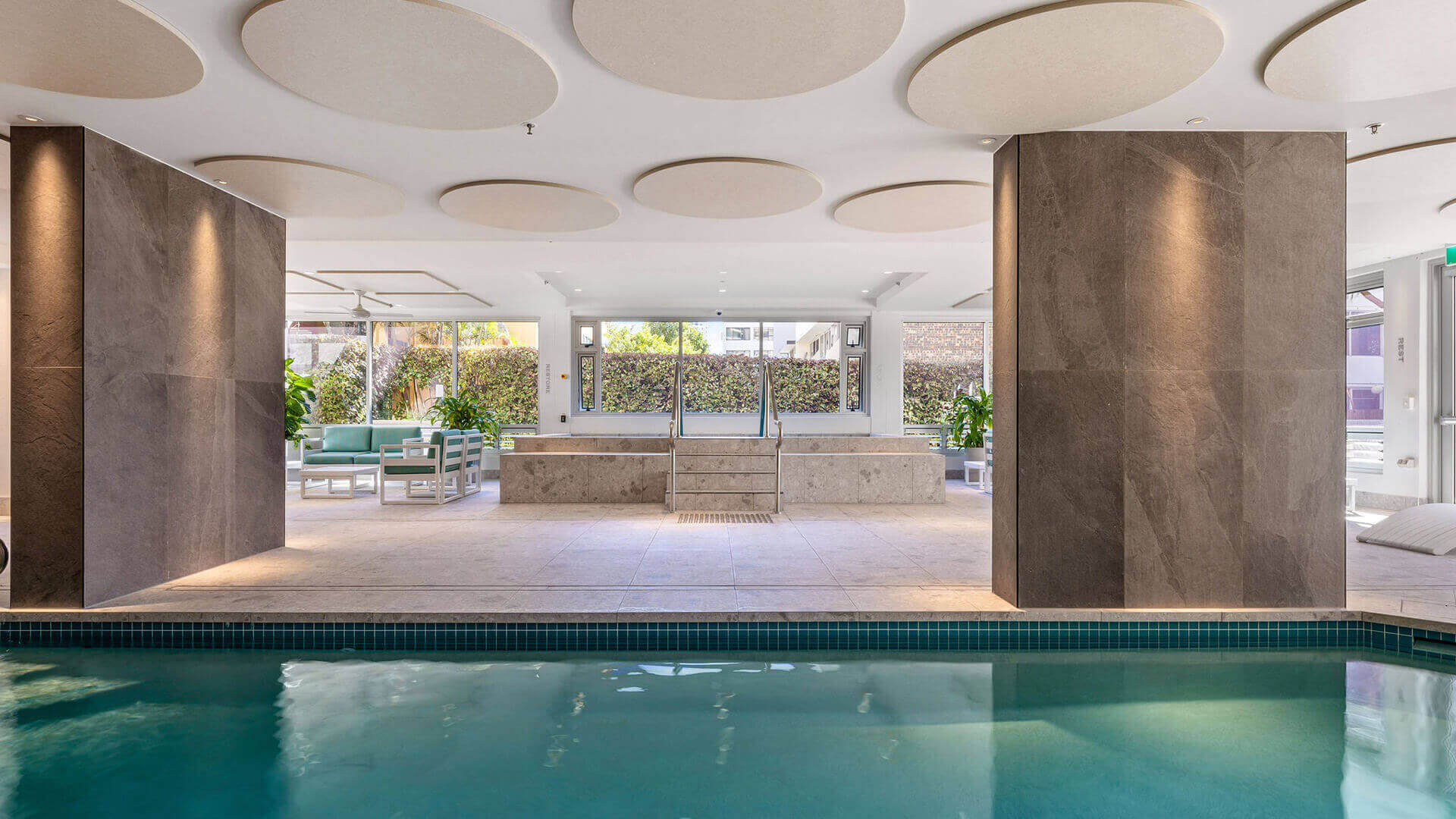 Heated indoor pool and spa area at ULTIQA Beach Haven, featuring elegant tiled finishes, lounge seating, and natural light - perfect for year-round relaxation.