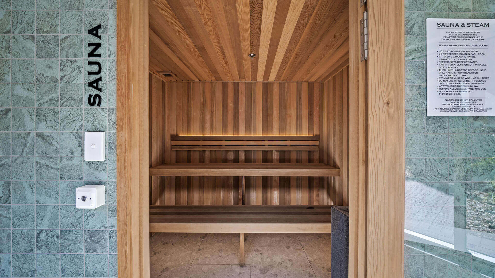 Modern cedar-lined sauna at ULTIQA Beach Haven, featuring tiered bench seating, tiled entrance wall and wellness guidelines for a rejuvenating relaxation experience.