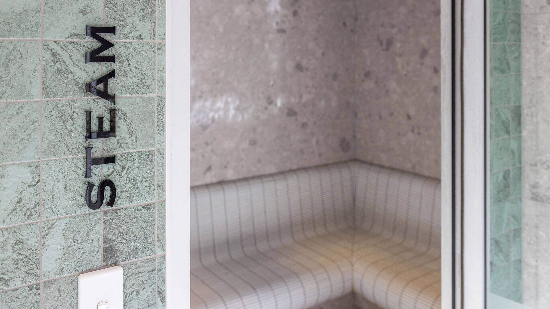 Modern tiled steam room at ULTIQA Beach Haven, featuring curved seating and soft lighting for a tranquil wellness experience.