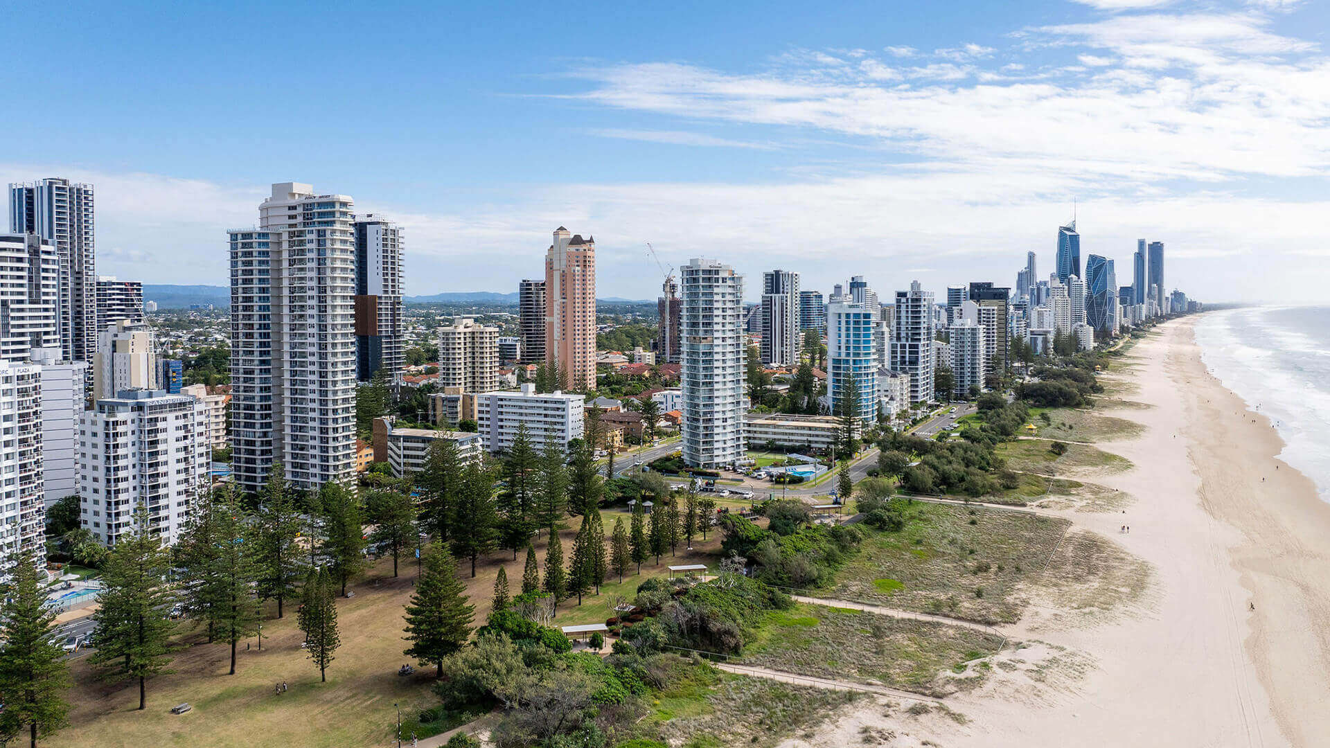 Scenic aerial view of Broadbeach on the Gold Coast, showcasing high-rise buildings, parklands and the expansive golden coastline stretching toward Surfers Paradise.
