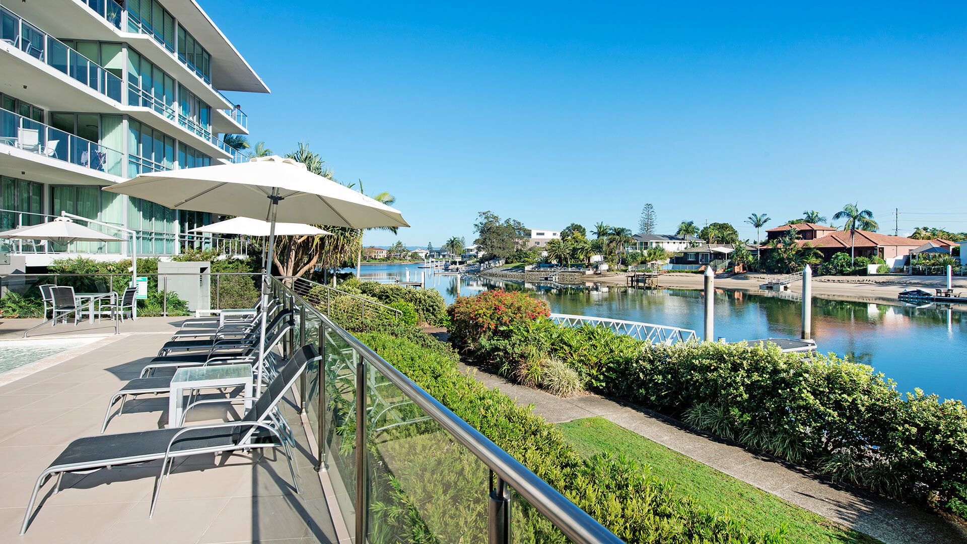 Waterside sun loungers with umbrellas at ULTIQA Freshwater Point Resort, Broadbeach.