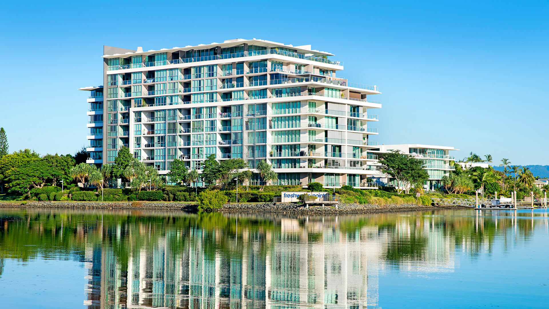 Waterfront exterior of ULTIQA Freshwater Point Resort, Broadbeach reflected in the calm river.
