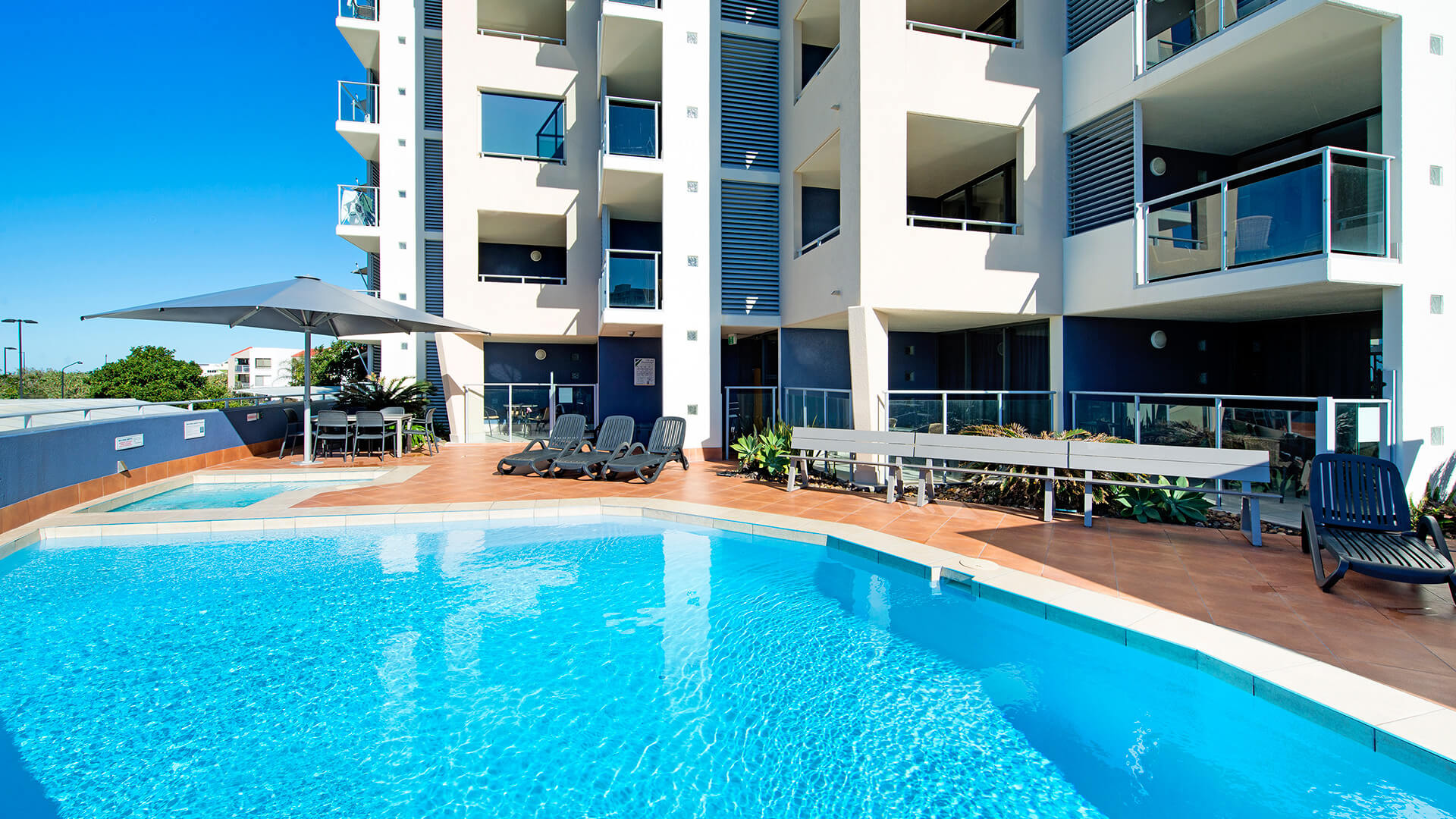 Outdoor swimming pool area with sun loungers and shaded seating at ULTIQA Shearwater Resort.