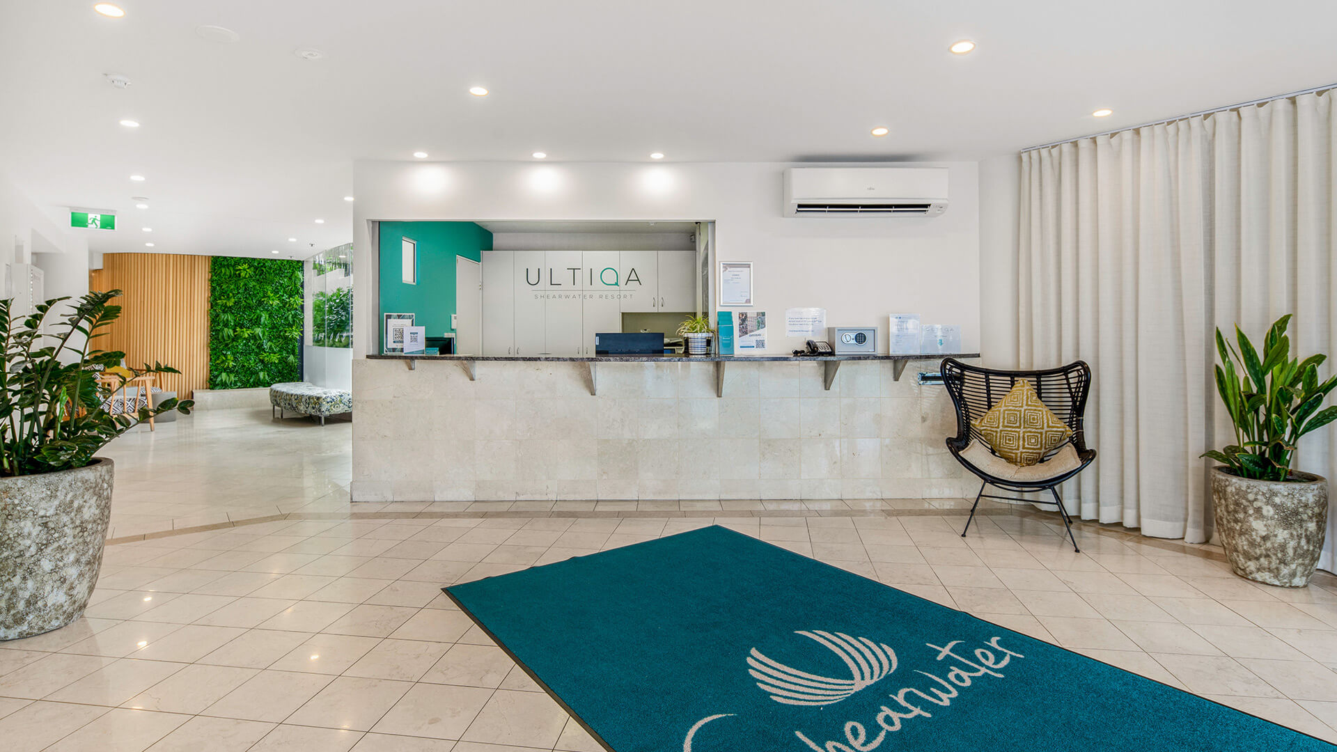 Reception area at ULTIQA Shearwater Resort featuring a modern front desk, indoor plants and a teal welcome mat with the Shearwater logo.
