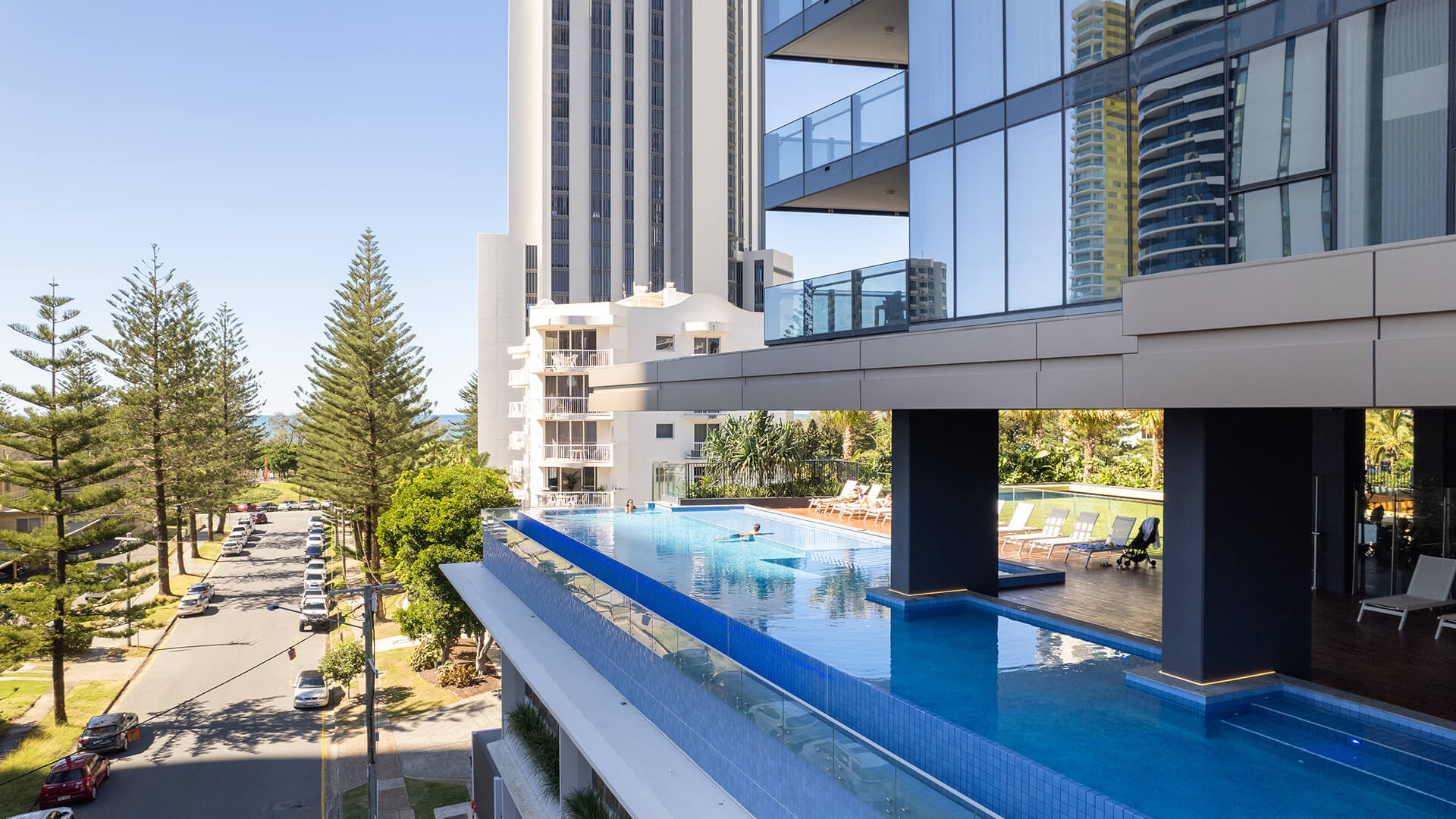 Infinity pool at ULTIQA Signature overlooking a tree-lined street leading towards the ocean.