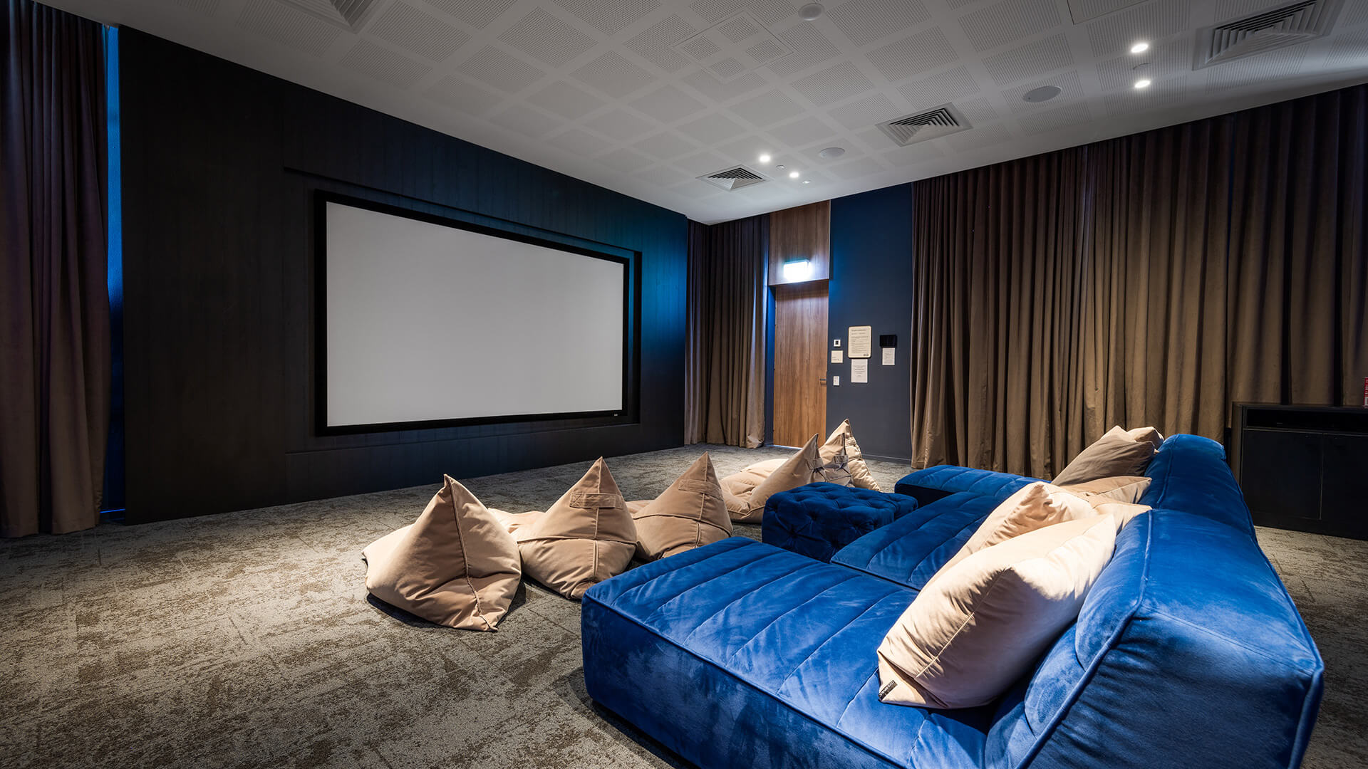 Private cinema room with a large screen, plush blue seating and bean bags at ULTIQA Signature.