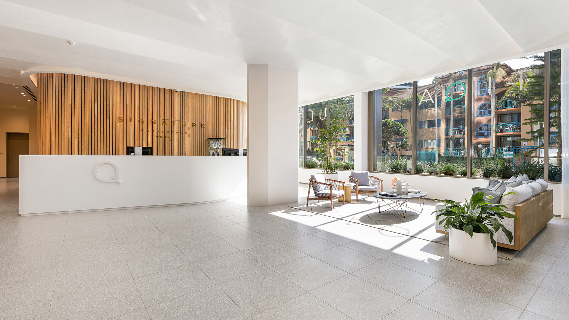Bright and modern hotel lobby at ULTIQA Signature with wooden accents, white furnishings and large windows.