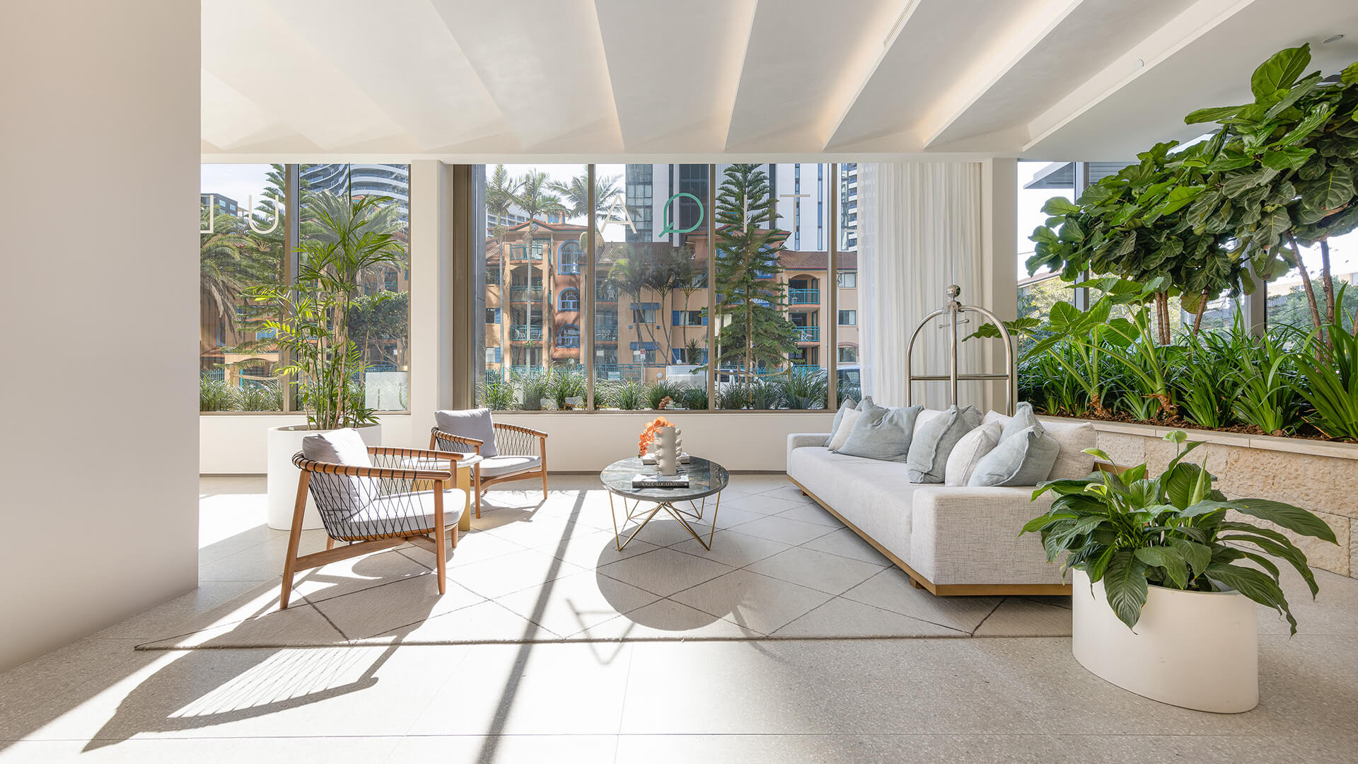 Sunlit lobby seating area with modern furniture, lush indoor plants and large windows at ULTIQA Signature.