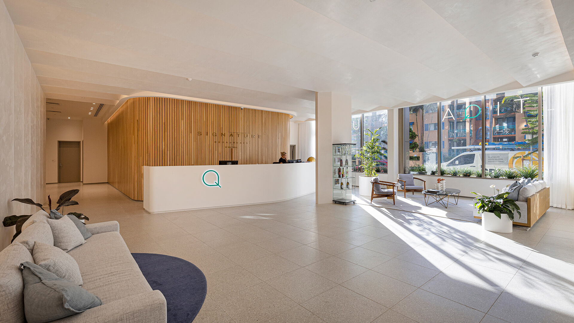 Spacious ULTIQA Signature lobby with a curved wooden reception desk, modern seating and floor-to-ceiling windows.