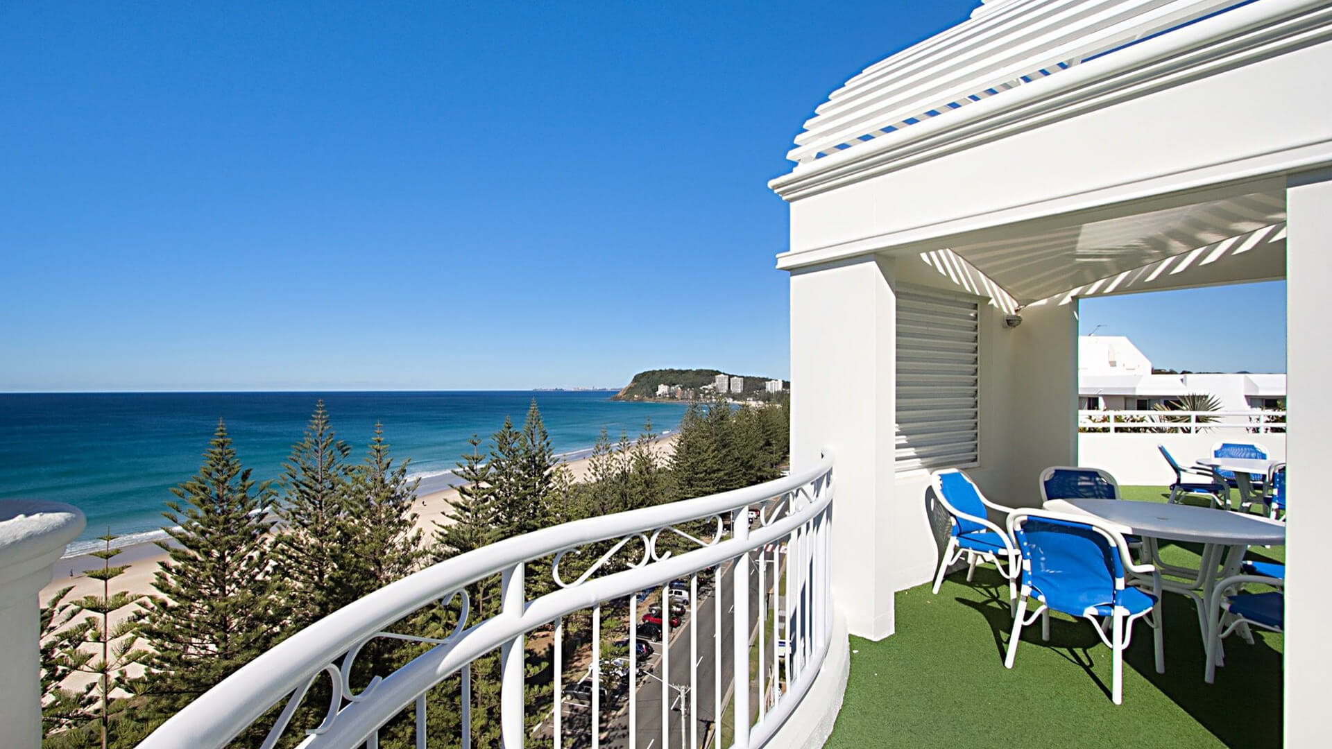 View from ULTIQA Burleigh Mediterranean Resort’s rooftop terrace, overlooking the pristine beach, ocean, and Burleigh Headland, with outdoor seating perfect for relaxing and enjoying the scenery.