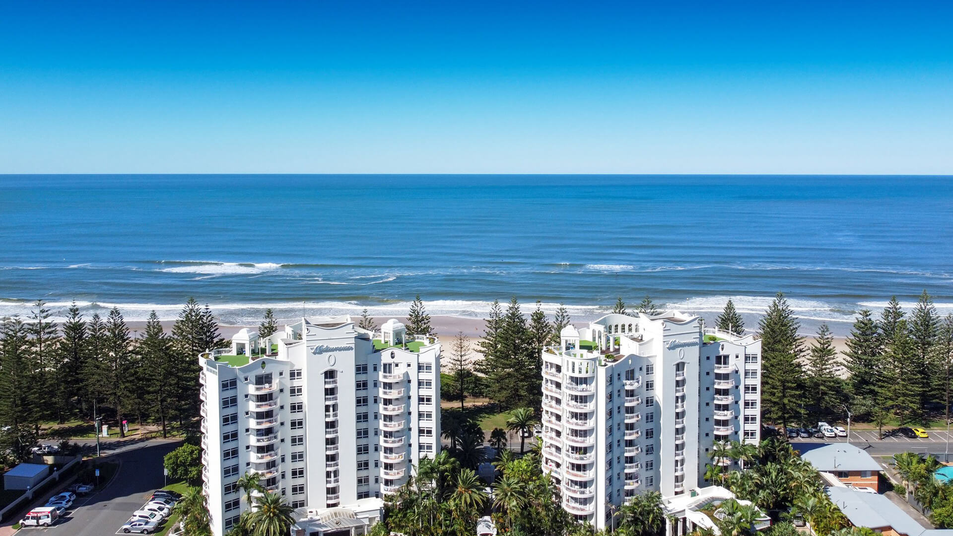 Aerial front view of ULTIQA Burleigh Mediterranean Resort showcasing its prime beachfront location, lush landscaping and uninterrupted ocean views.