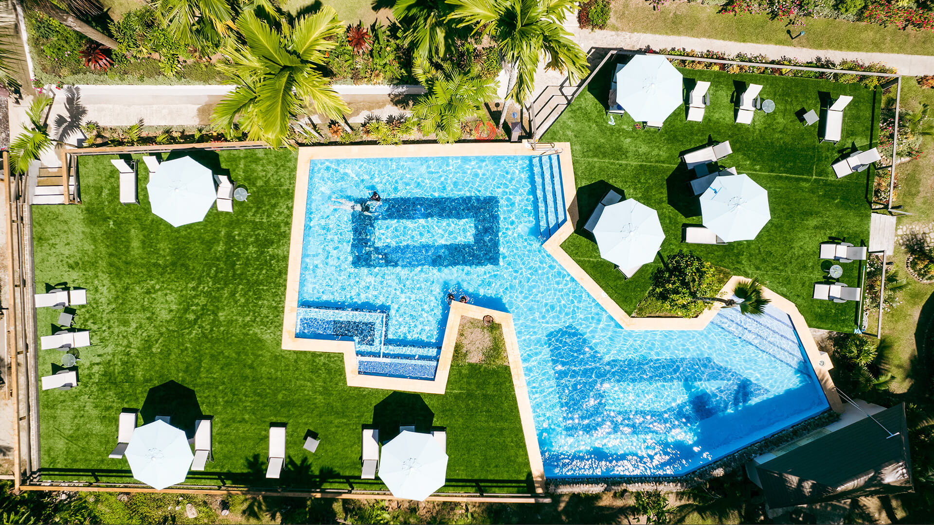 Aerial top view of resort pool at ULTIQA Fiji with sun loungers, umbrellas and tropical landscaping.
