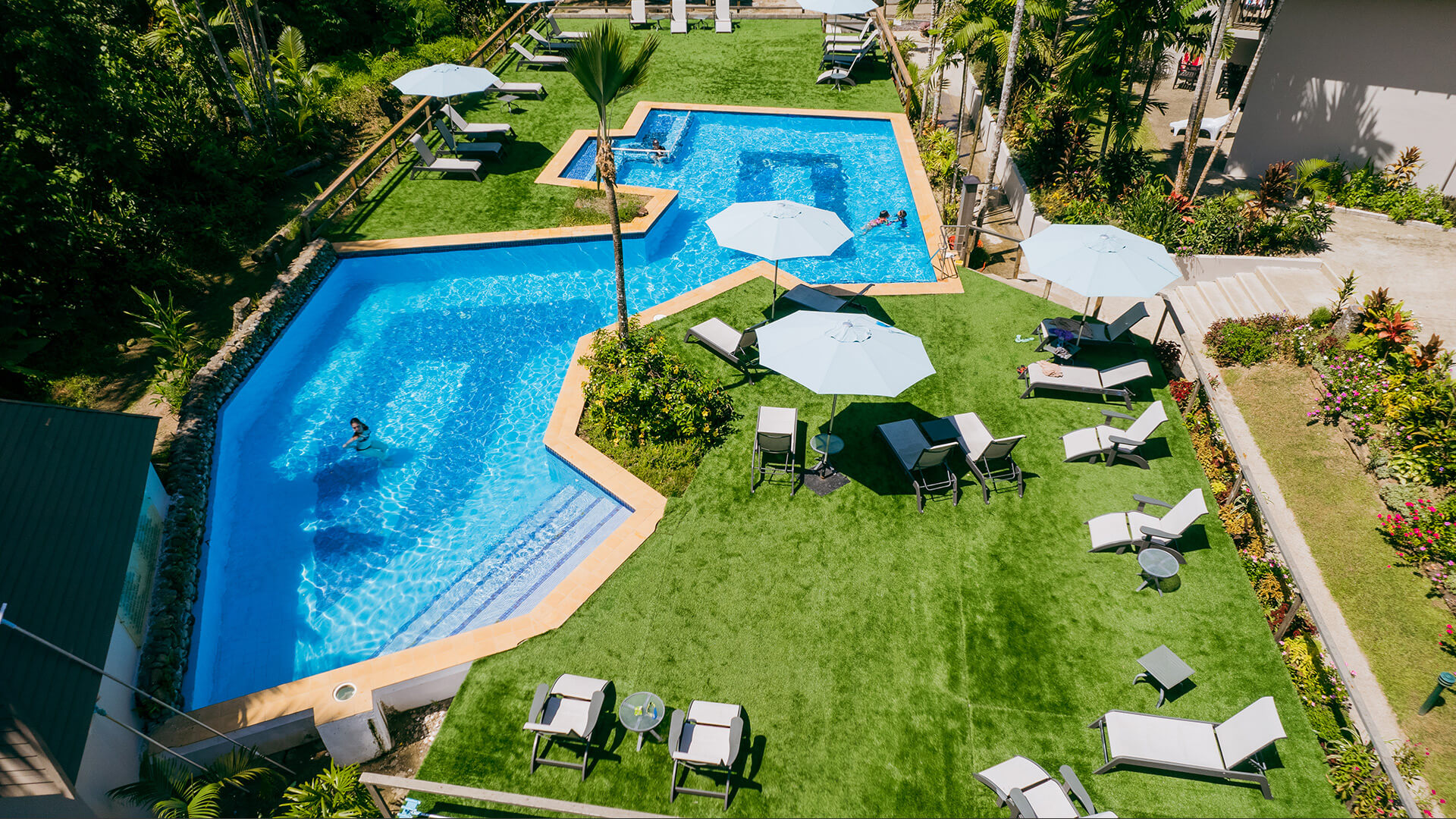 Aerial view of swimming pool at ULTIQA Fiji with sun loungers, umbrellas and surrounding tropical gardens.