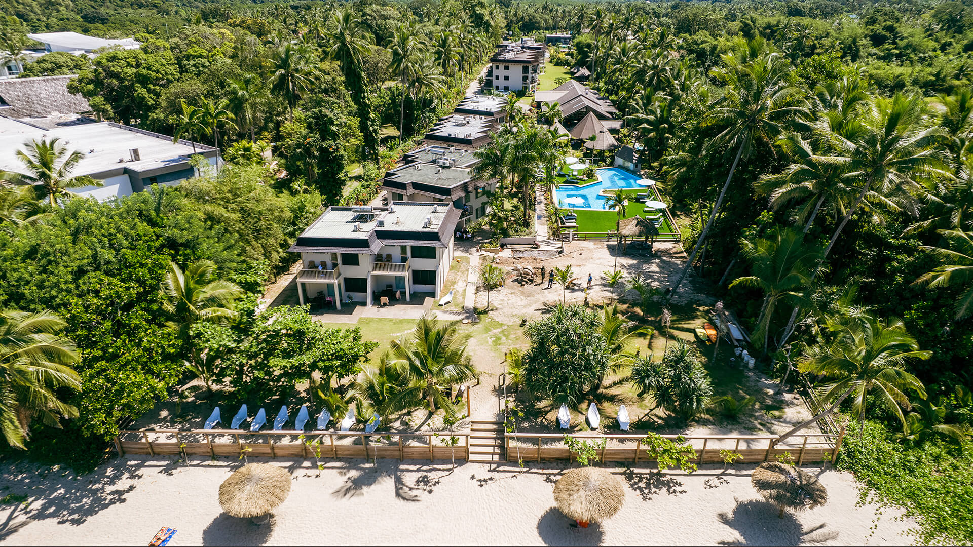 Aerial view of ULTIQA Fiji resort from beachfront, showing accommodation buildings, pool area and tropical gardens.