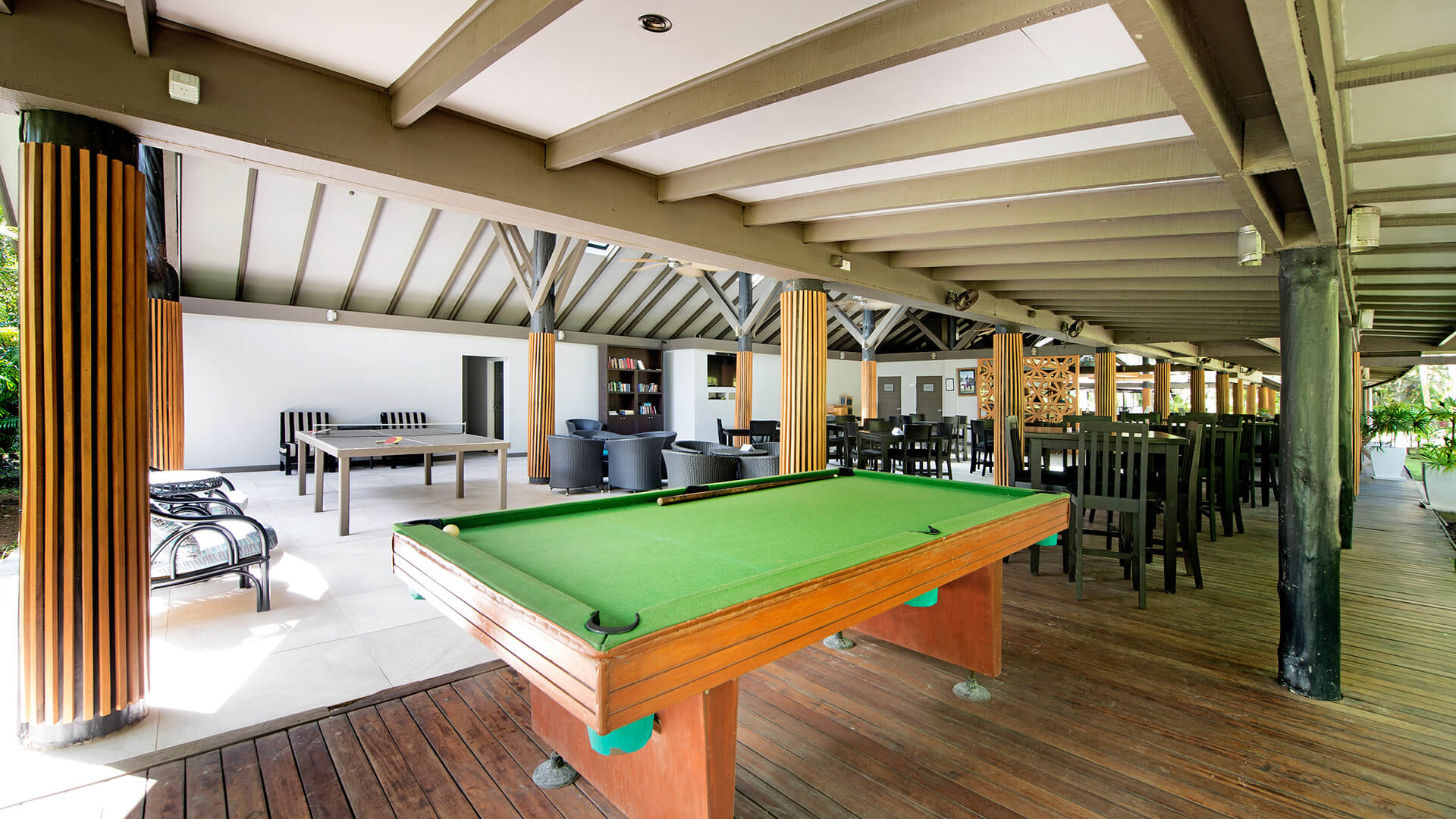 Open-air recreation area at ULTIQA Fiji featuring a pool table, lounge chairs and dining tables with a tropical backdrop.