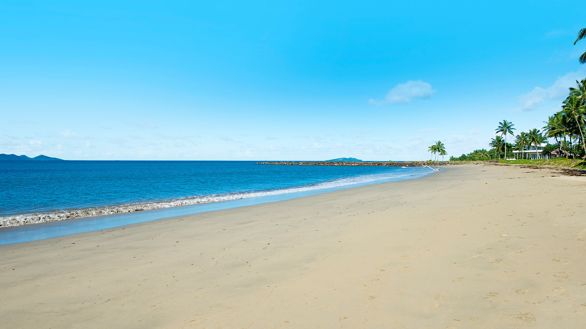 Wide stretch of golden sandy beach with gentle waves, lined with palm trees and ocean views at ULTIQA Fiji Palms Beach Resort.