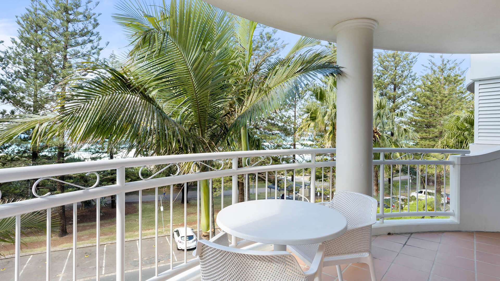 Private balcony featuring outdoor seating and views of lush palms and the nearby ocean.