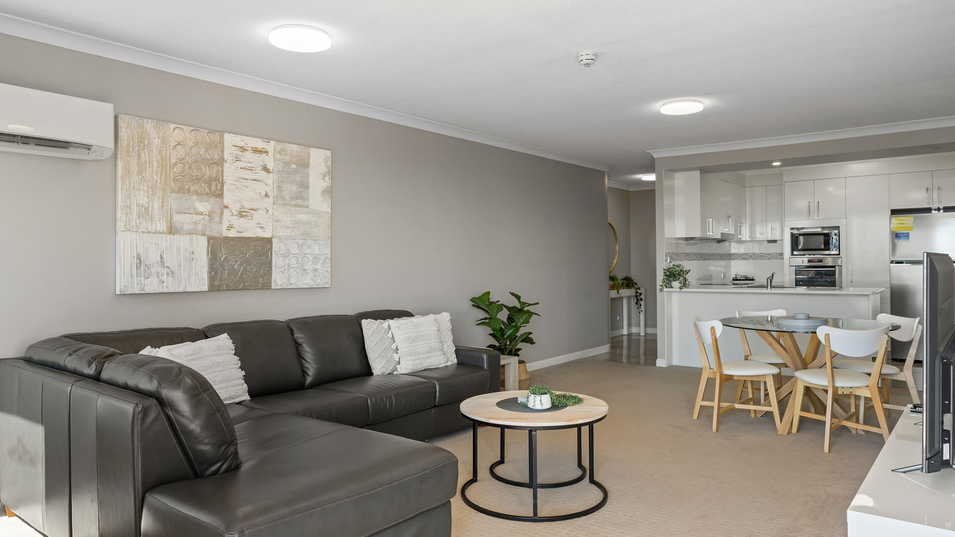 Spacious open-plan living area with leather lounge and dining table in 2 Bedroom Garden View Apartment at ULTIQA Burleigh Mediterranean Resort.