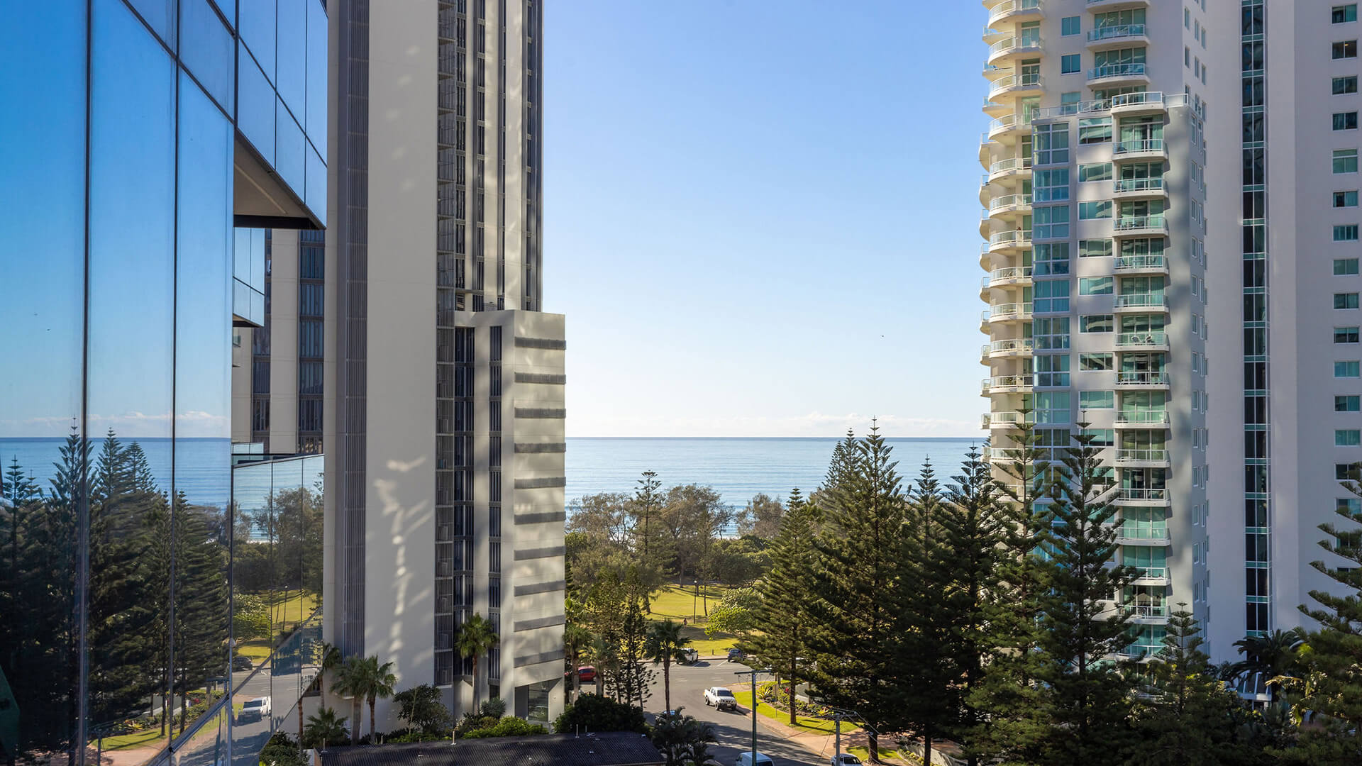 Ocean view framed by high-rise buildings and pine trees from ULTIQA Signature at Broadbeach.