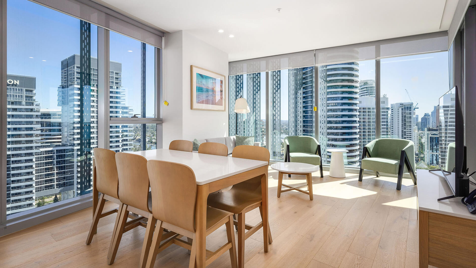 Dining and living area, featuring a wooden dining set, green armchairs, and floor-to-ceiling windows with city views.