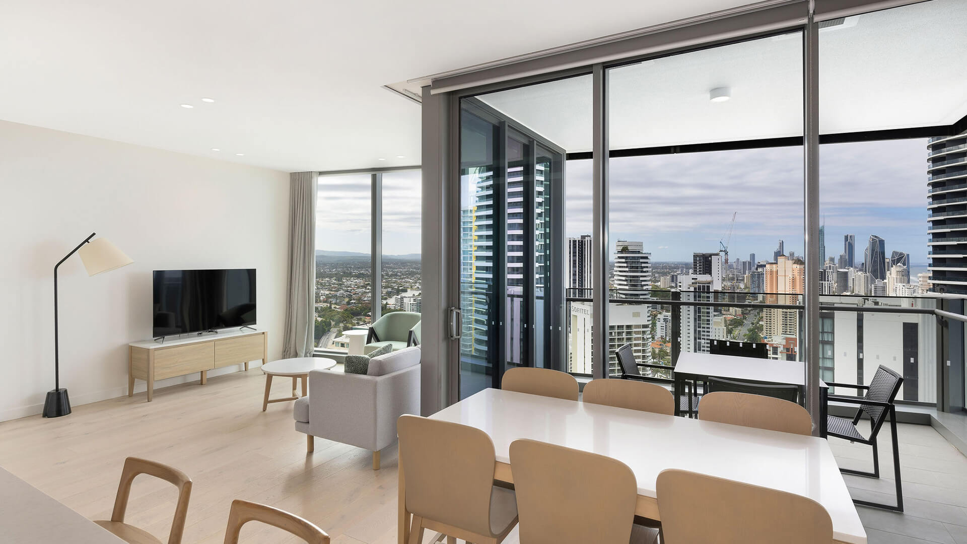 Dining area with seating for six, flowing into a modern lounge and private balcony with panoramic city views in the 2 Bedroom Skyhome at ULTIQA Signature at Broadbeach.