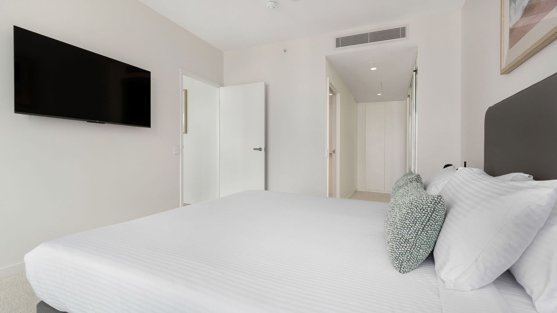 Master bedroom with king bed, wall-mounted TV, and access to hallway in the 2 Bedroom Skyhome at ULTIQA Signature at Broadbeach.
