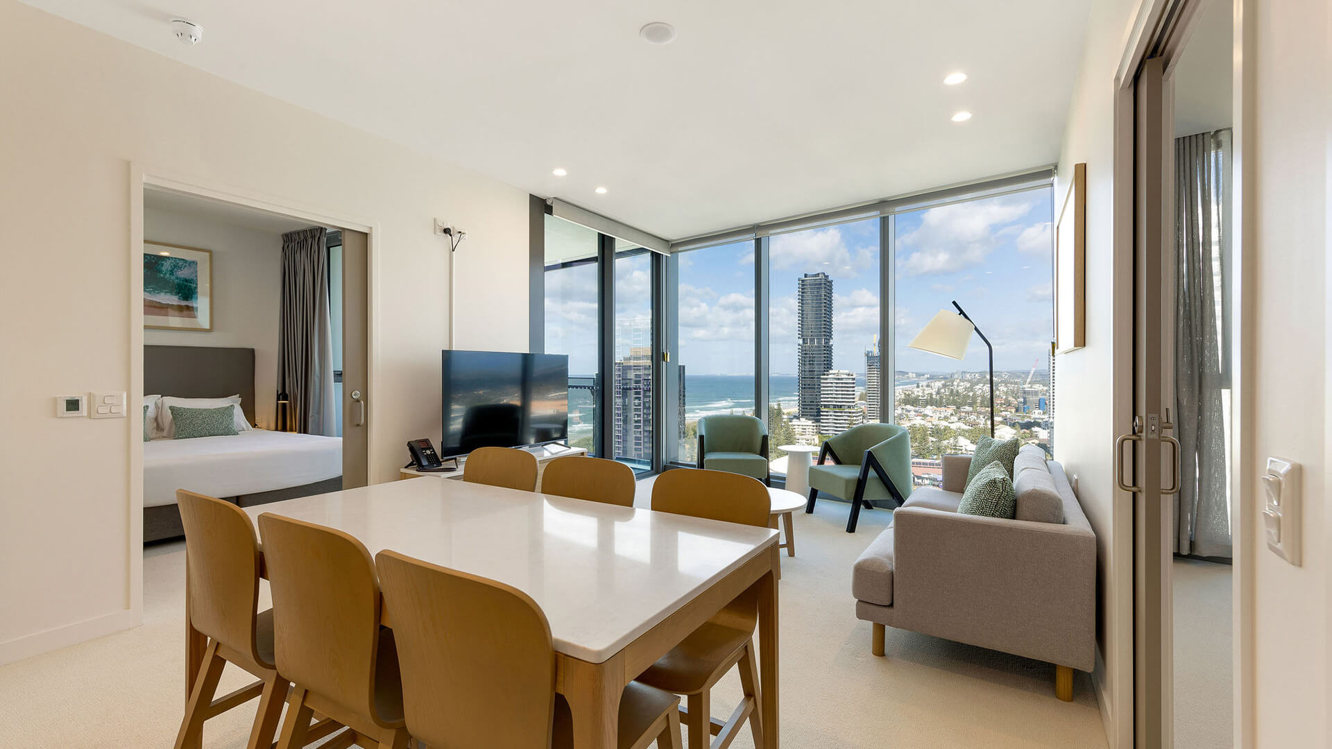Dining and living area with floor-to-ceiling windows and city views in 2 Bedroom Accessible Suite at ULTIQA Signature at Broadbeach.
