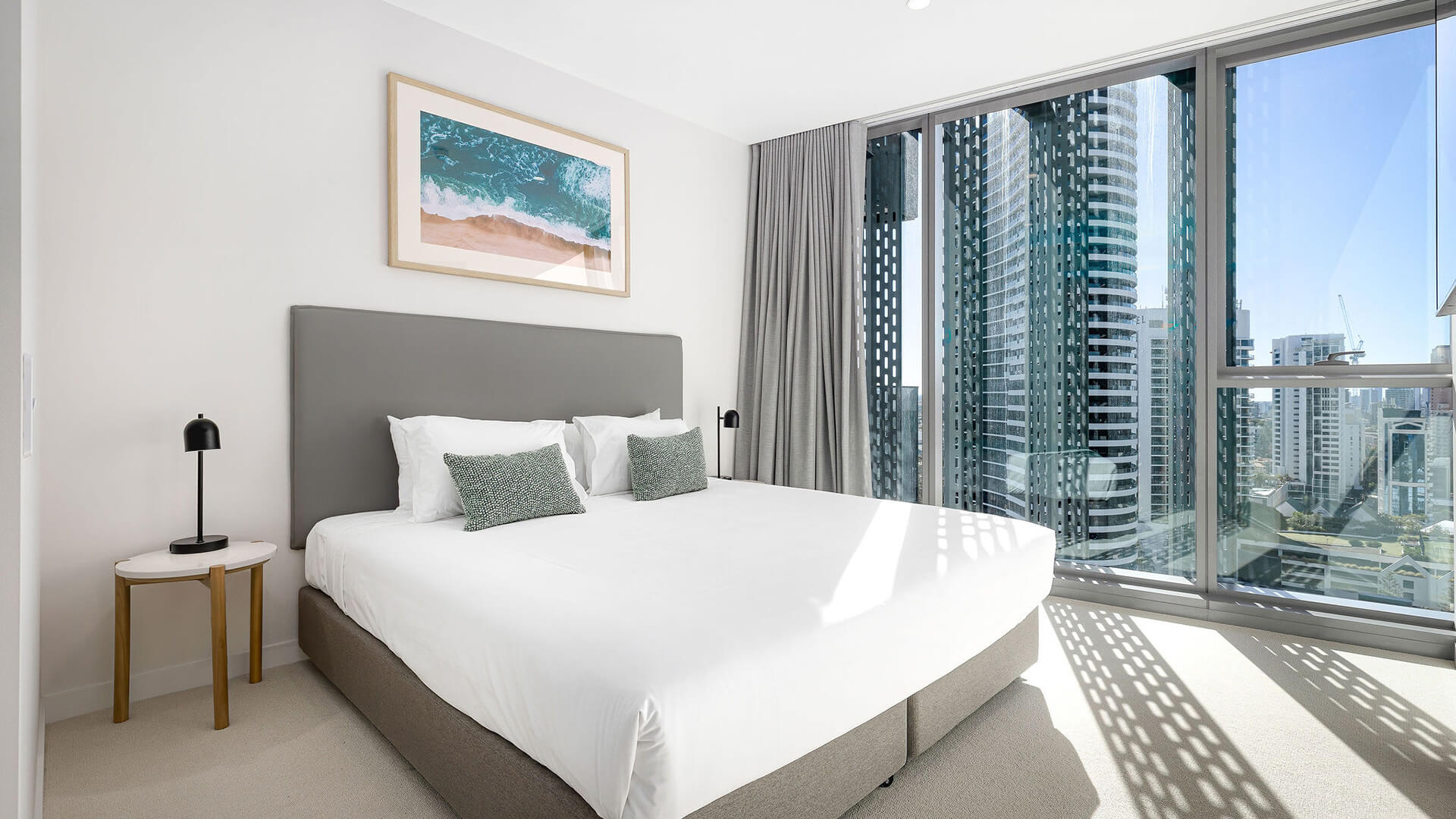 Bedroom in 3 Bedroom Suite at ULTIQA Signature, featuring a large bed, beach artwork, and city views through floor-to-ceiling windows.