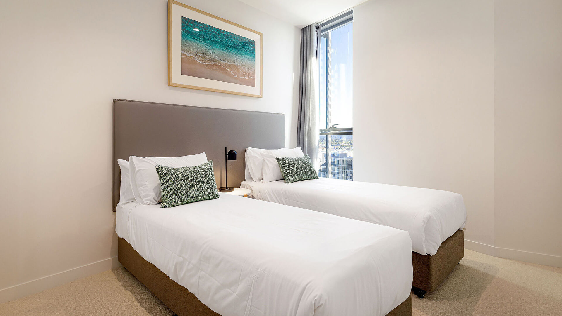 Twin bedroom in 3 Bedroom Suite at ULTIQA Signature, featuring two single beds, beach artwork, and large window with natural light.