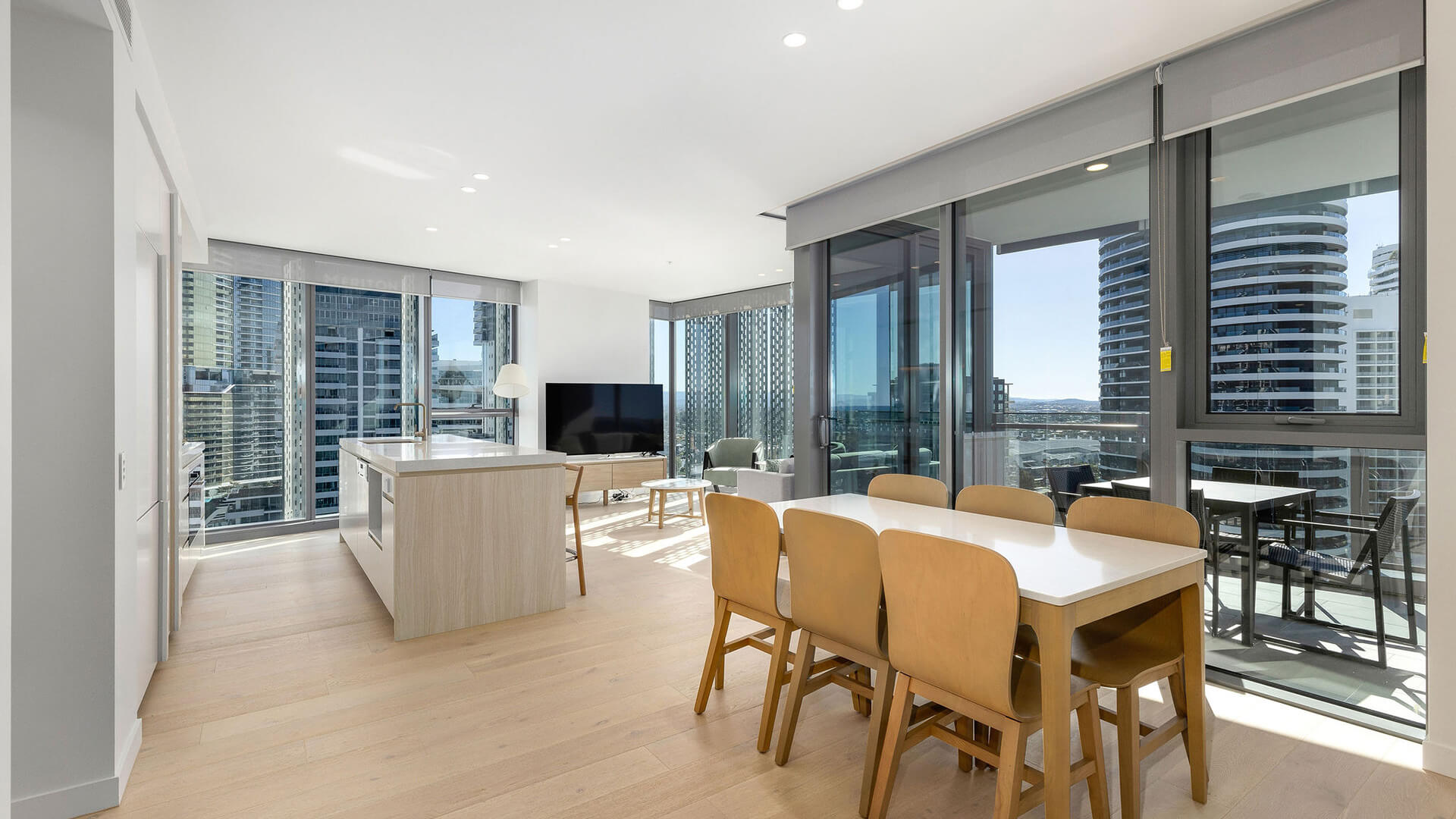 Open-plan living area in 3 Bedroom Suite at ULTIQA Signature, featuring kitchen, dining table, and lounge with city views through large windows.