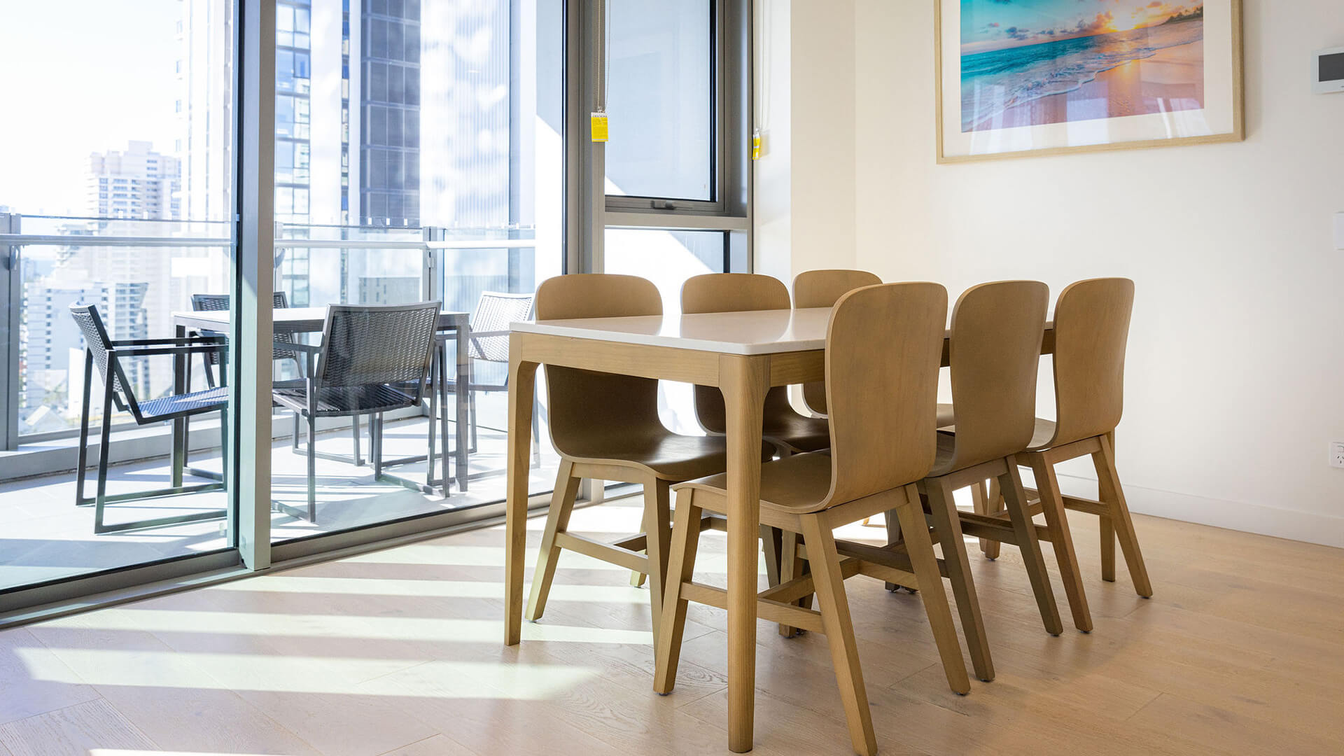Dining area in 3 Bedroom Suite at ULTIQA Signature, with wooden table, balcony seating, and city views through glass doors.