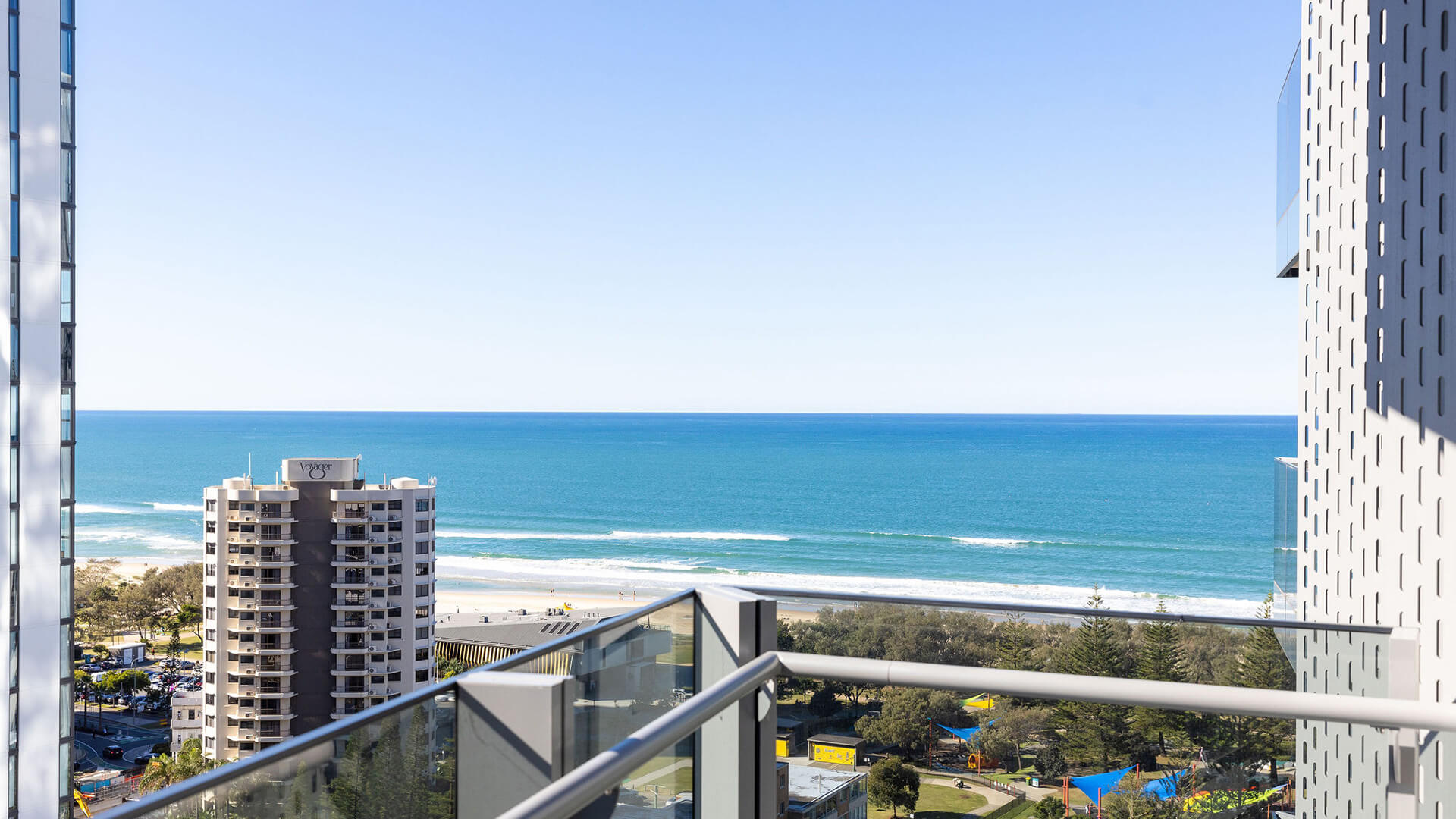 Balcony view from 3 Bedroom Suite at ULTIQA Signature, showing Wyndham building, ocean waves, sandy beach, and clear blue sky.