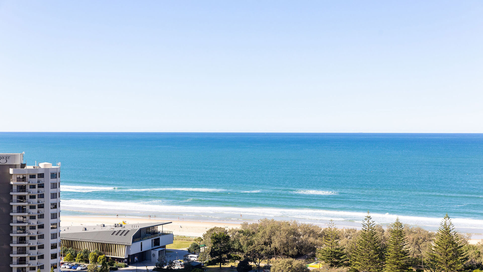 View from 3 Bedroom Suite at ULTIQA Signature, showing beach, ocean, and nearby buildings under a clear blue sky.