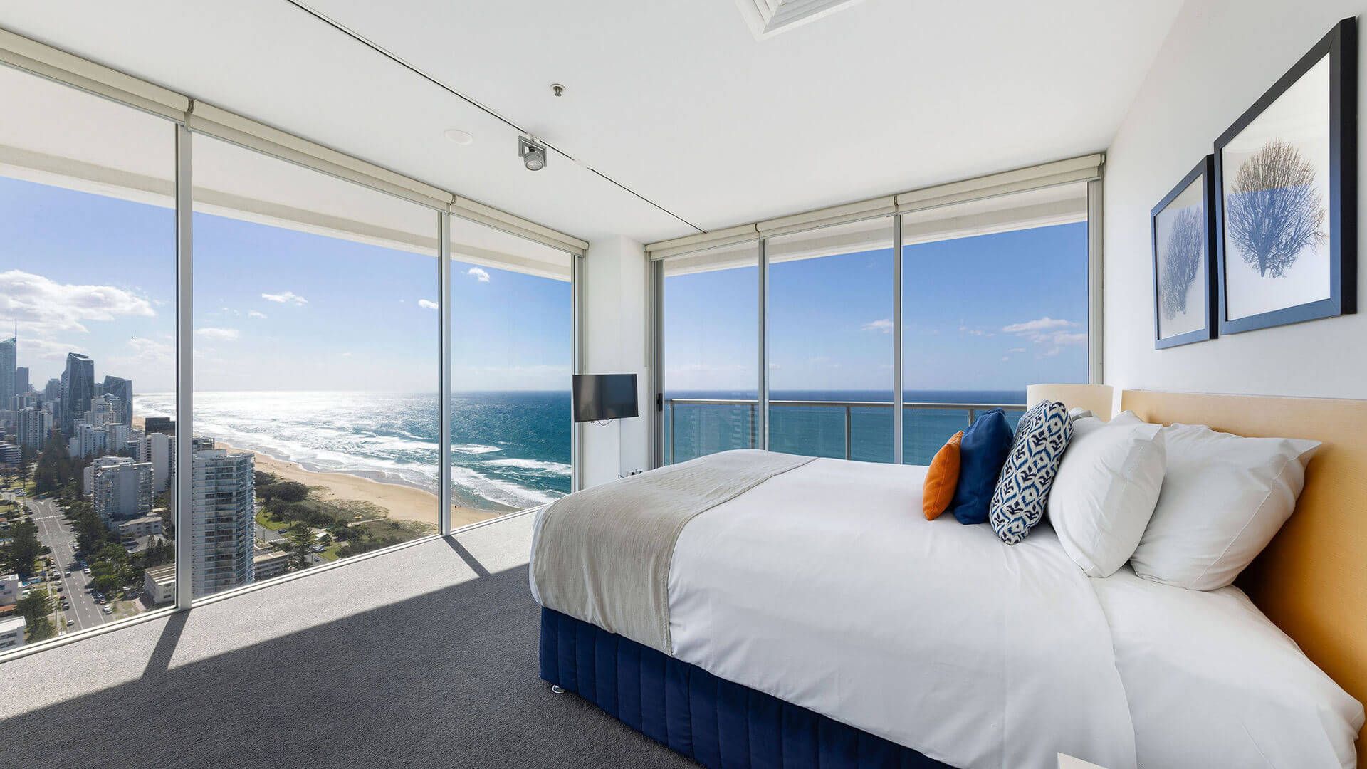 Master bedroom in ULTIQA Air’s 3 Bedroom Ocean View Suite featuring a king bed, wall-mounted TV, and floor-to-ceiling windows with panoramic ocean and city views.