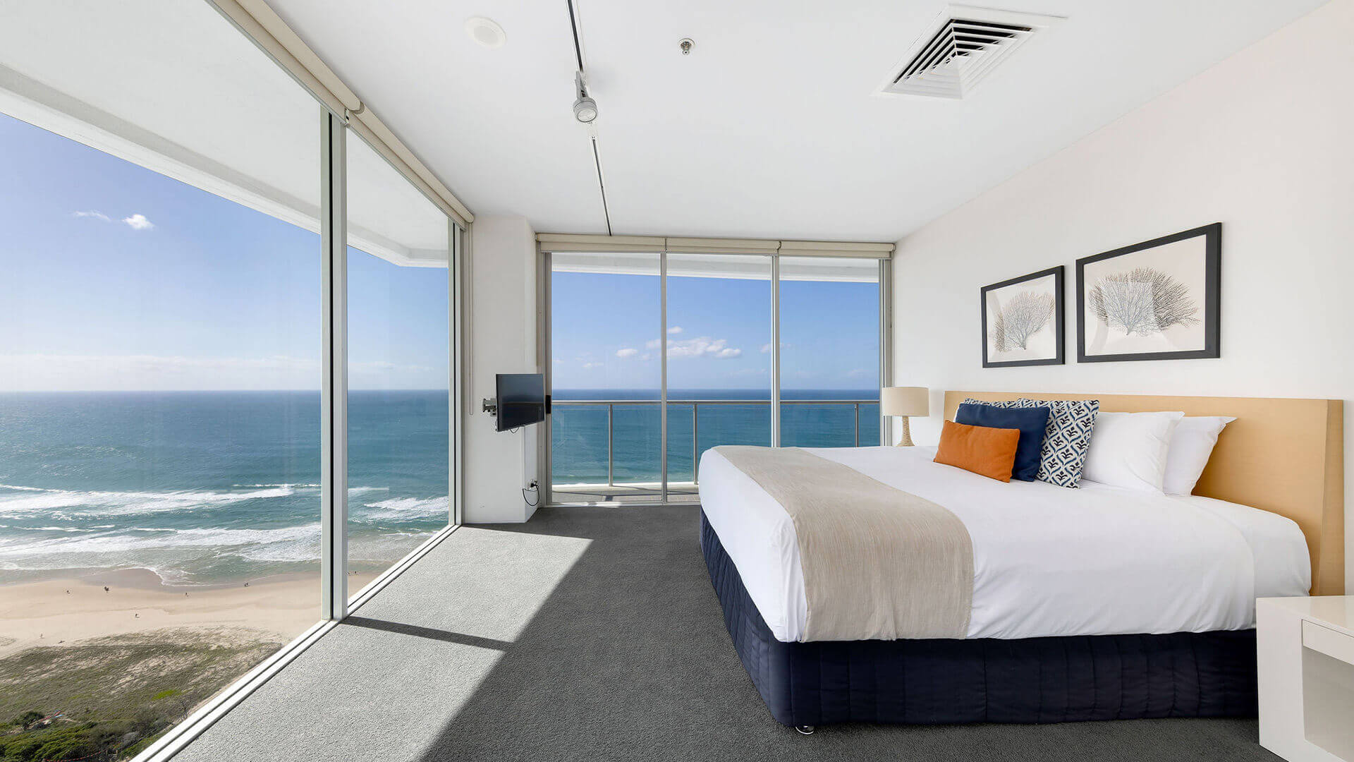 Ocean-facing bedroom in ULTIQA Air’s 3 Bedroom Ocean View Suite with king bed, abstract wall art, and panoramic beach views through floor-to-ceiling windows.