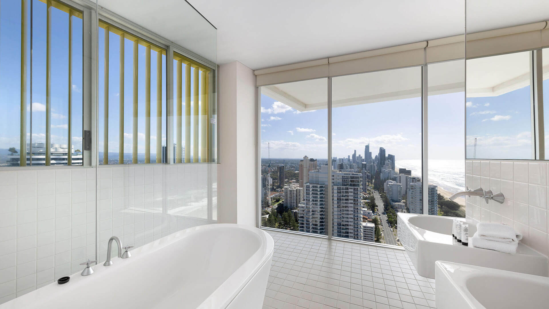 : Luxury ensuite in ULTIQA Air’s 3 Bedroom Ocean View Suite featuring a freestanding bathtub, dual sinks, and floor-to-ceiling windows with sweeping ocean and city views.