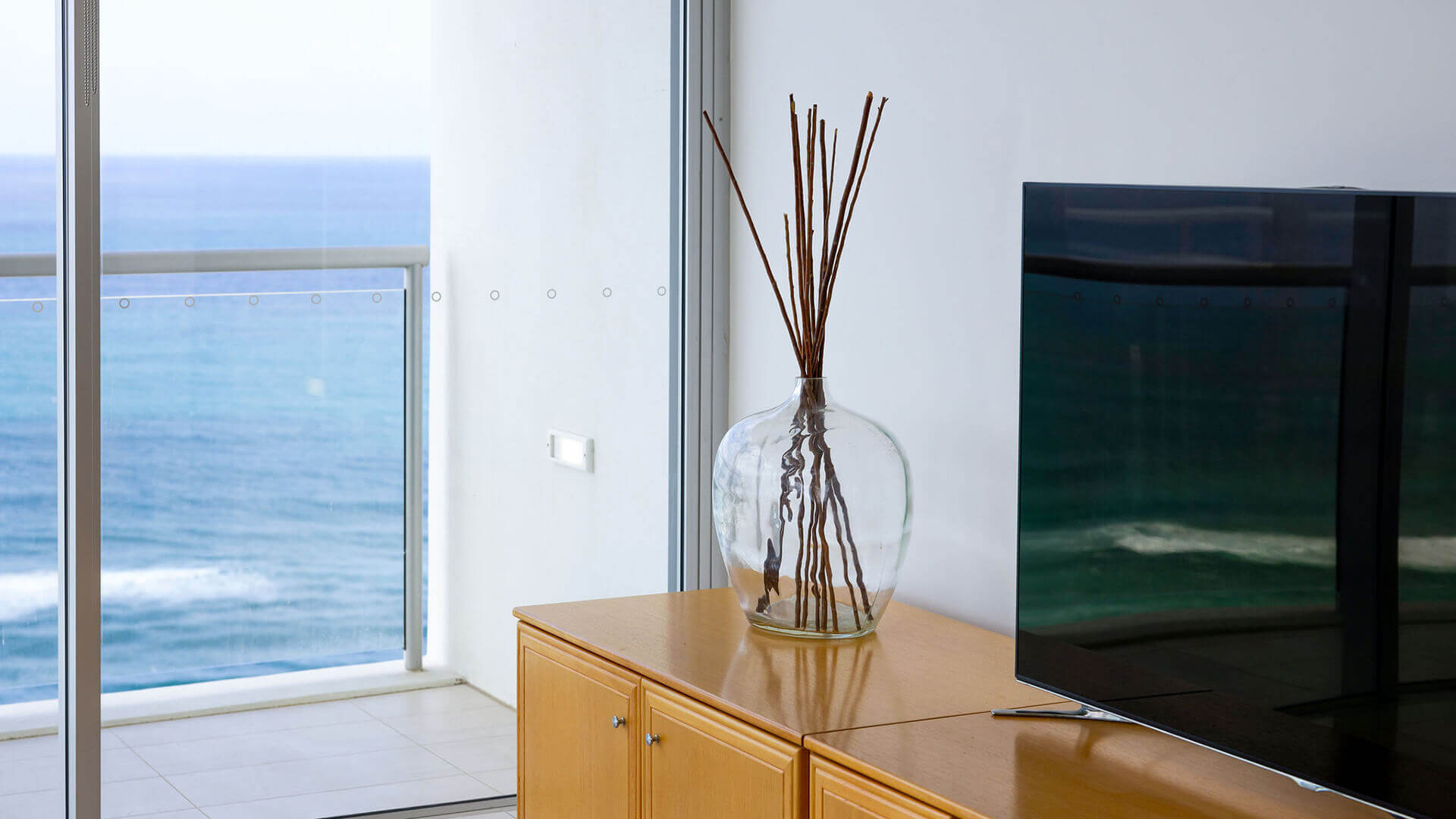 Ocean-view lounge in ULTIQA Air’s 3 Bedroom Ocean View Suite featuring minimalist décor, a flat-screen TV, and balcony access through floor-to-ceiling glass doors.