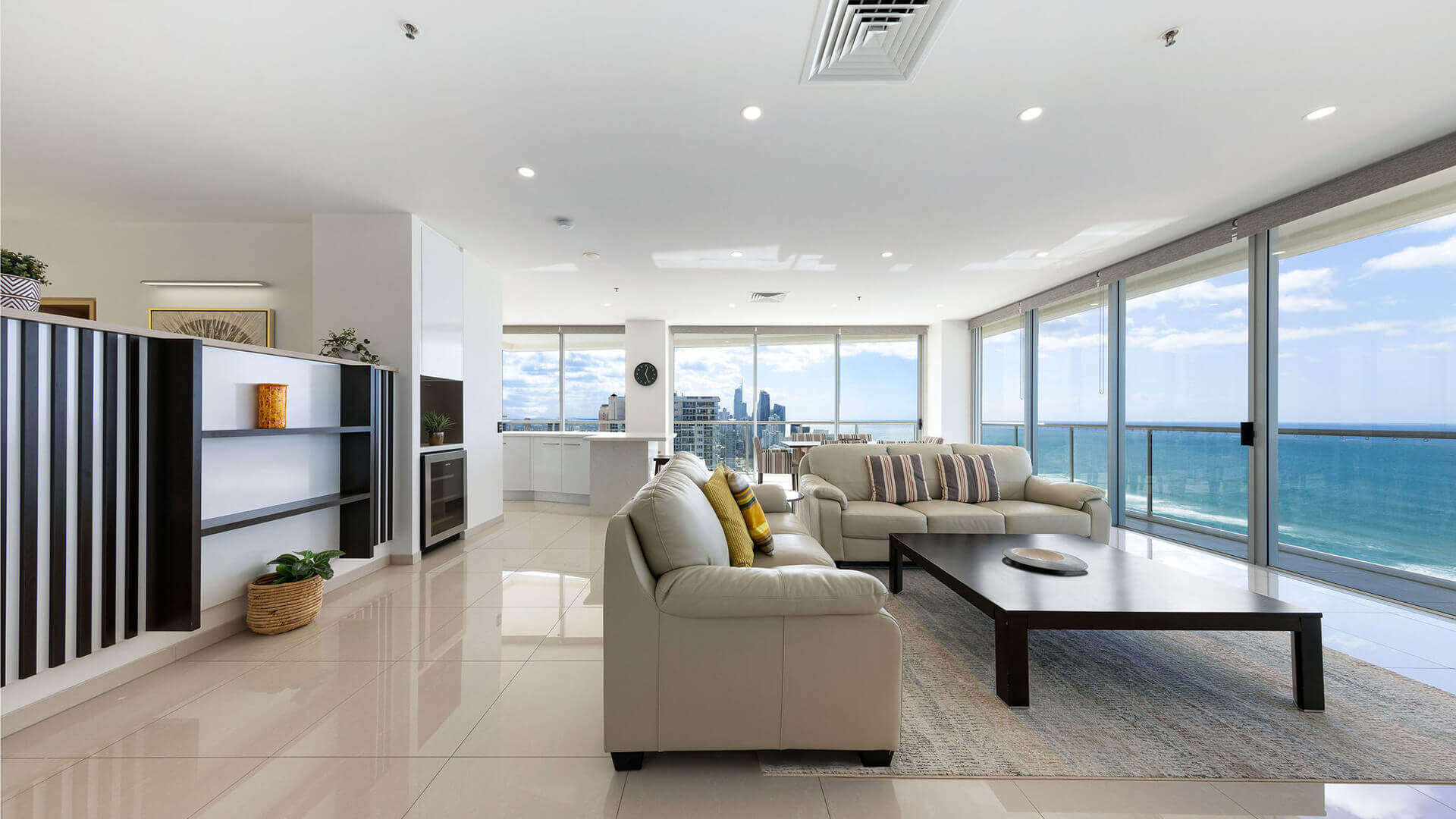 Spacious living area in ULTIQA Air’s 3 Bedroom Ocean View Suite featuring beige sofas, a dark wood coffee table, and panoramic ocean and city views through floor-to-ceiling windows.