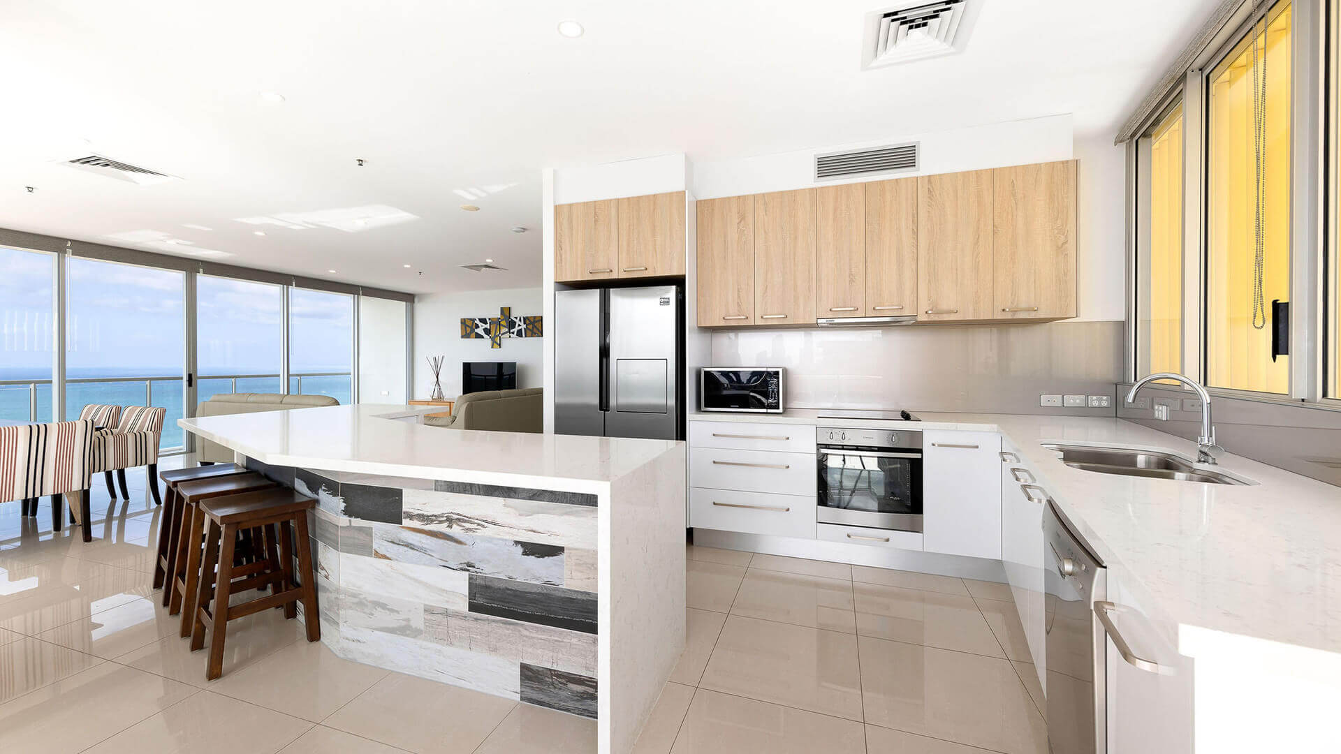 Kitchen and dining area with island bench, wood cabinetry, and ocean views in ULTIQA Air’s 3 Bedroom Ocean View Suite.