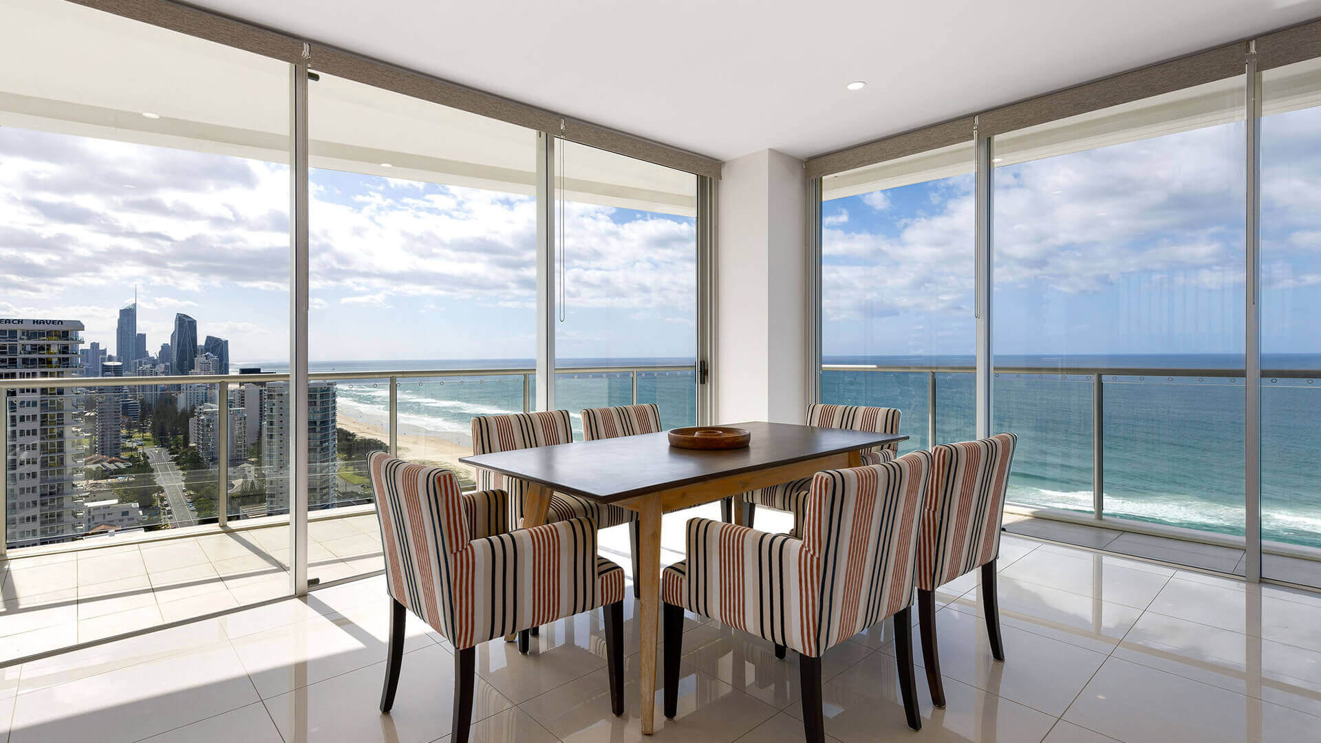 Dining area with striped chairs and ocean views in ULTIQA Air’s 3 Bedroom Ocean View Suite.