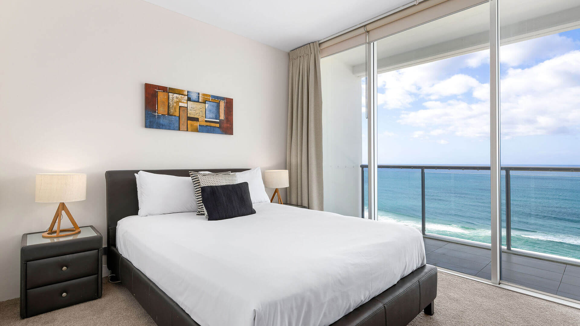Bedroom with white linens, abstract art, and ocean-view balcony in ULTIQA Air’s 3 Bedroom Ocean View Suite.