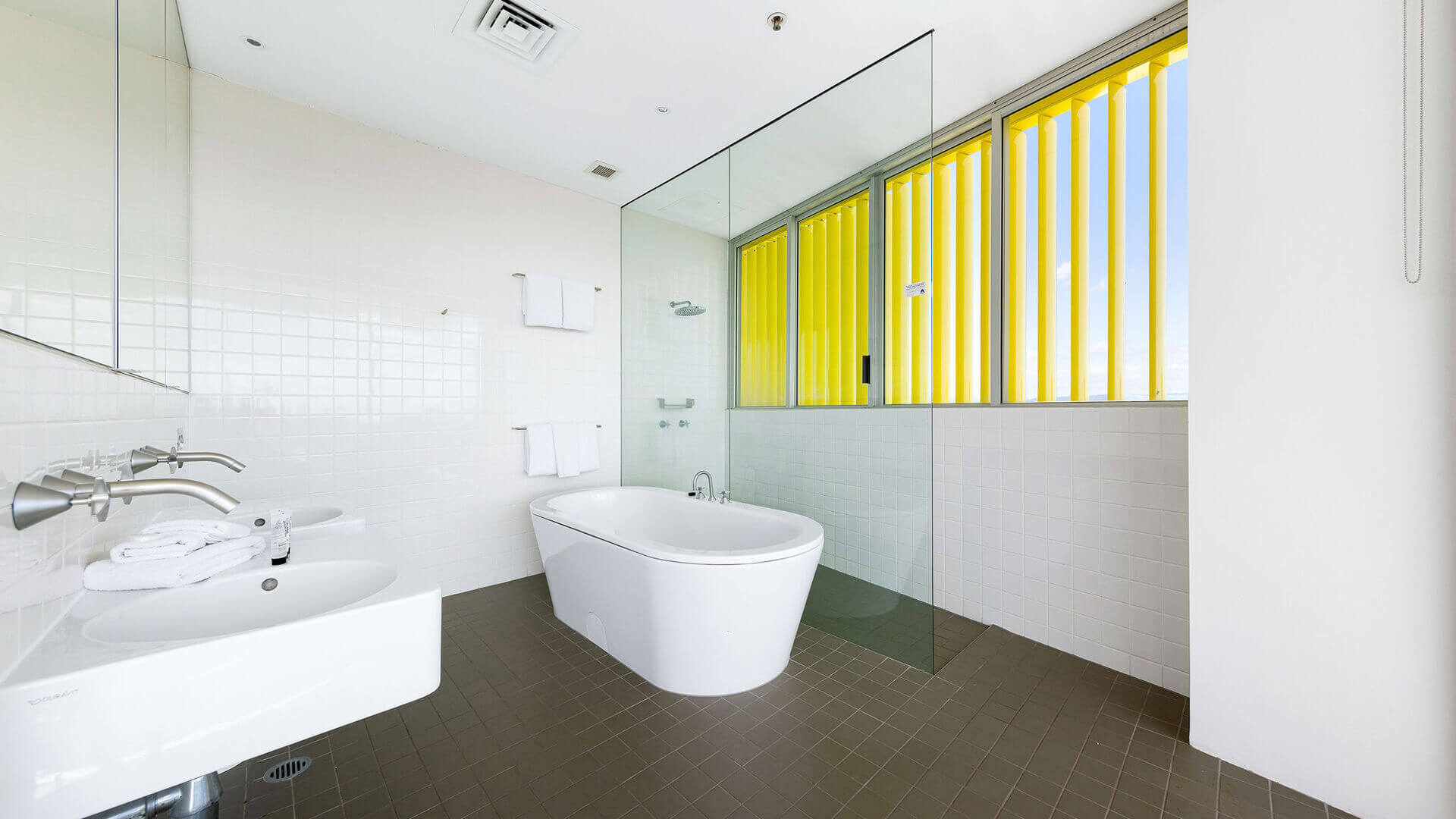Bathroom with white bathtub, glass partition, and brown tile flooring in ULTIQA Air’s 3 Bedroom Ocean View Suite.