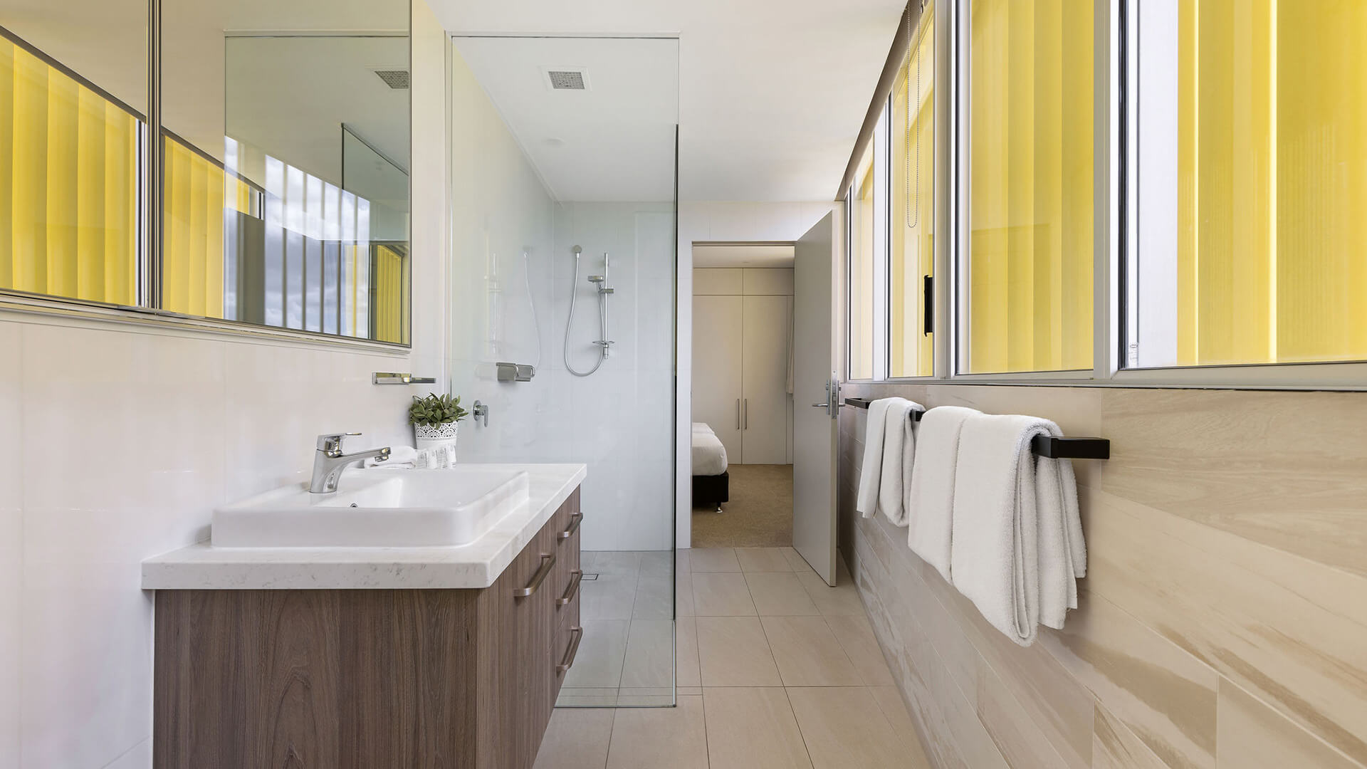 Bathroom with wood vanity, glass shower, and beige tiles in ULTIQA Air’s 3 Bedroom Ocean View Suite.